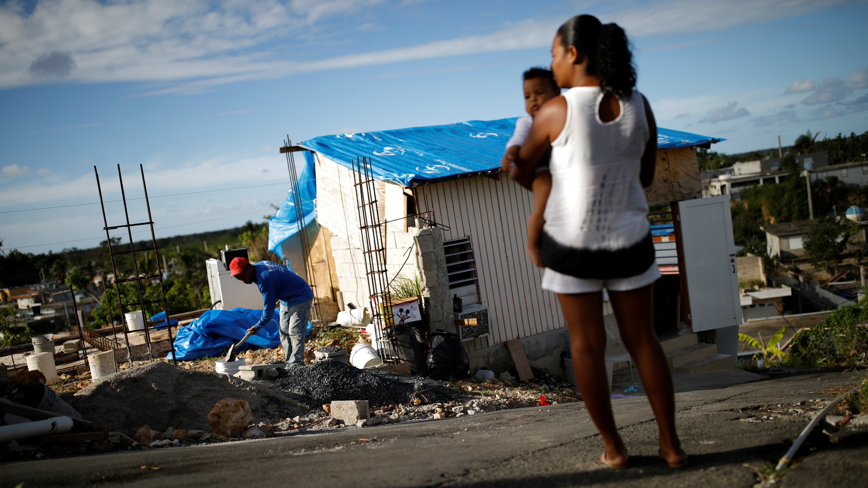 a woman holds a child in front of destroyed building