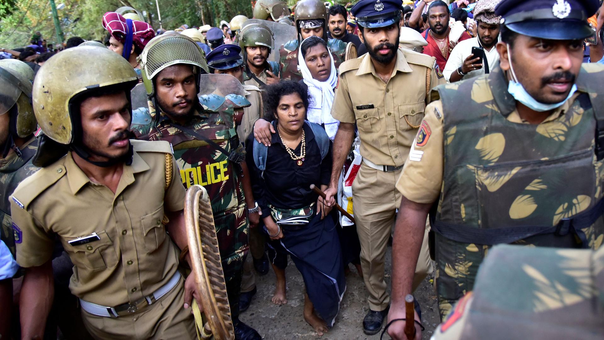 A crowd of people, some wearing police hats or helmets, surround two women