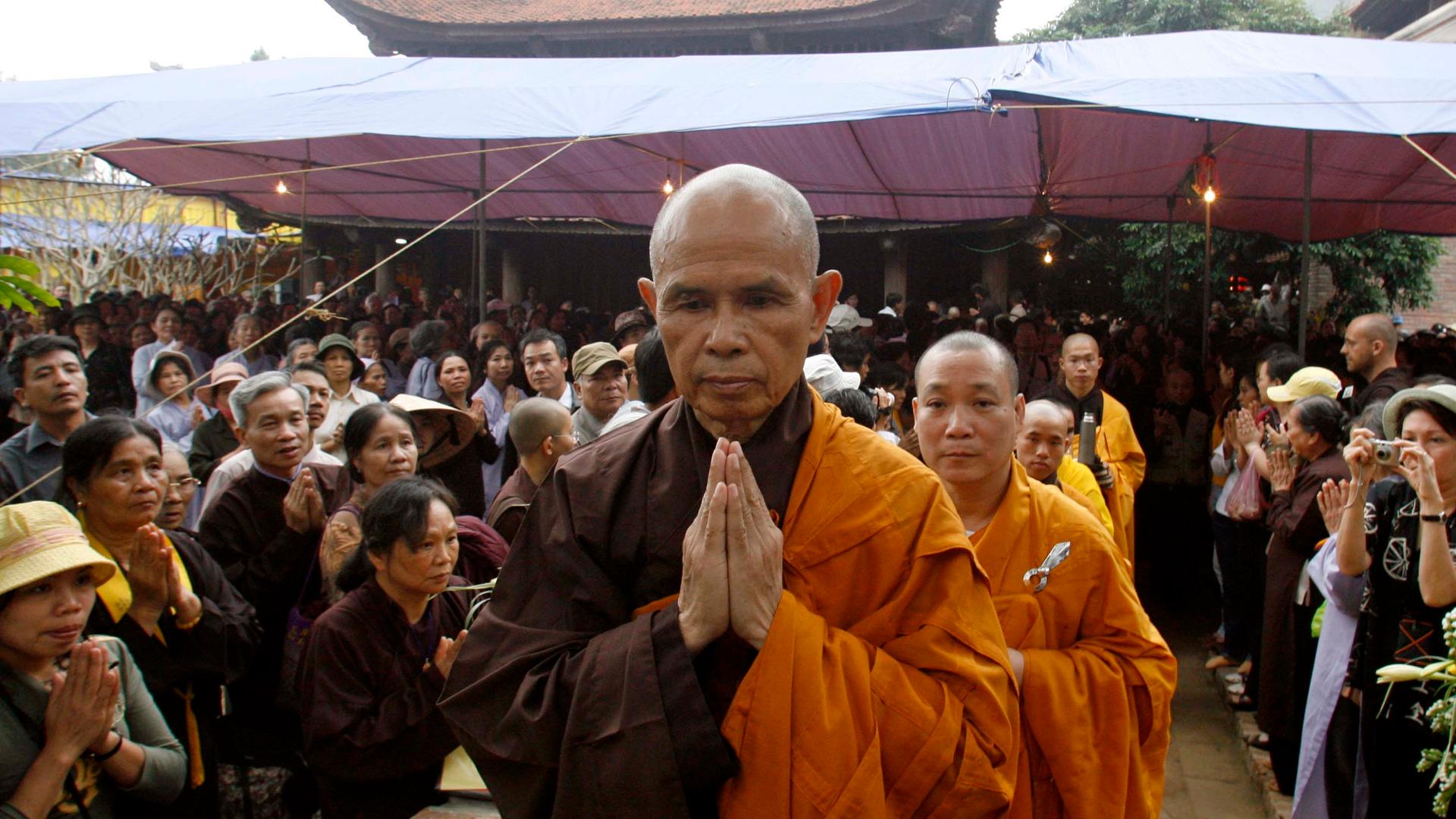 A Buddhist monk walks through a crowd with his hands in a prayer position