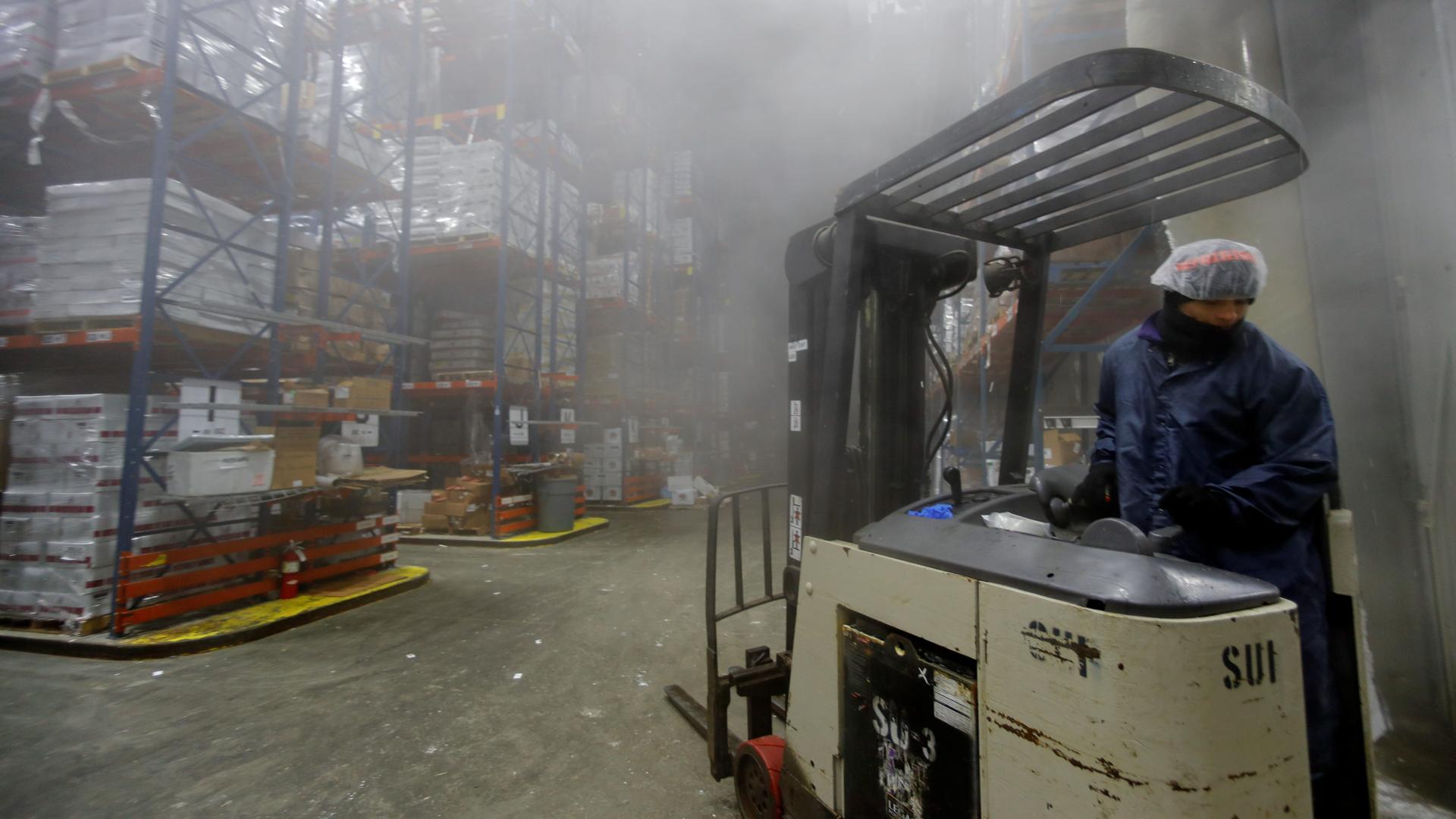 a man operates a forklift with rows of boxes in the background