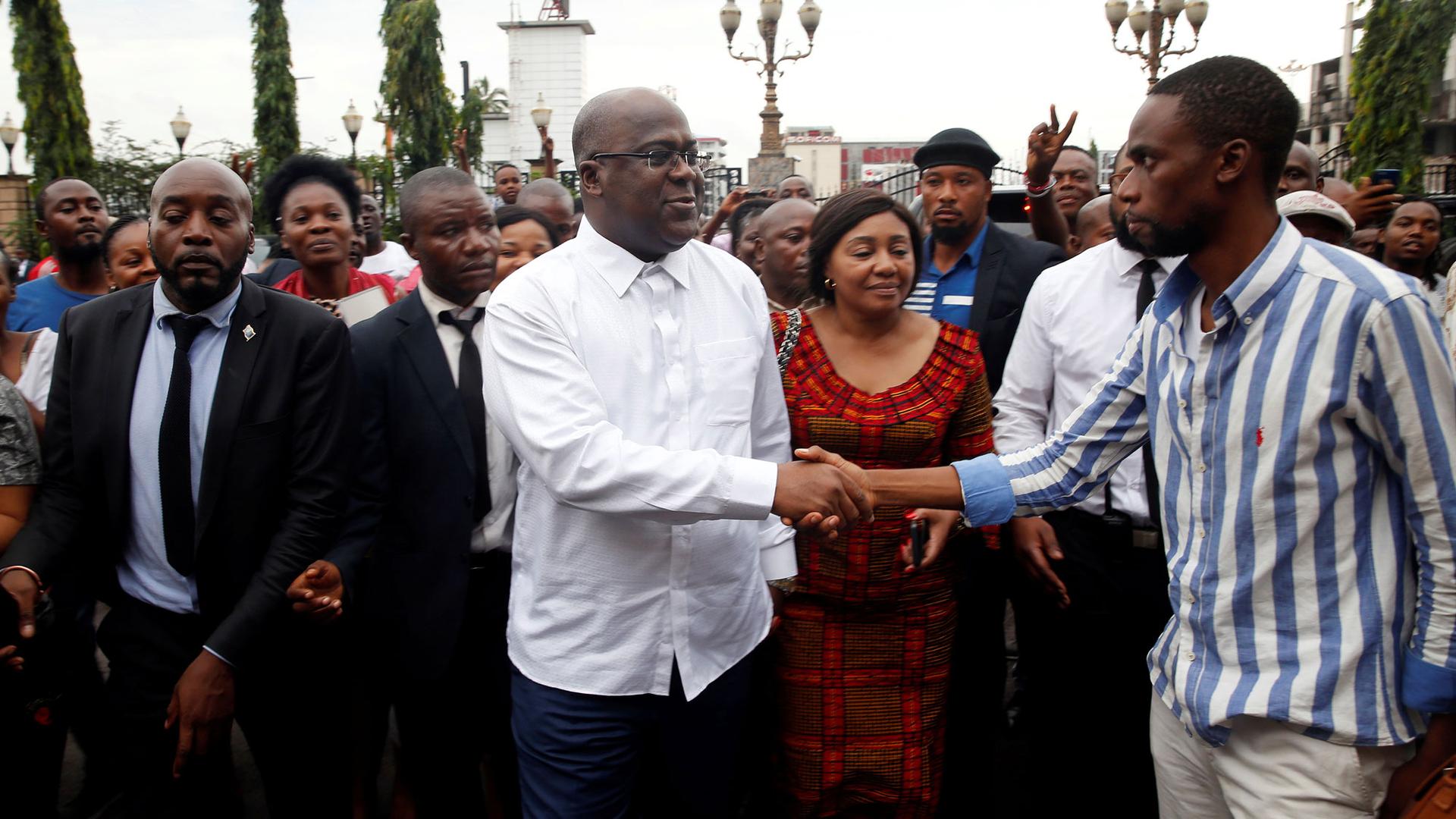 Felix Tshisekedi is shown in a white shirt shaking hands with a suppoert in the streets of Kinshasa, Democratic Republic of Congo.