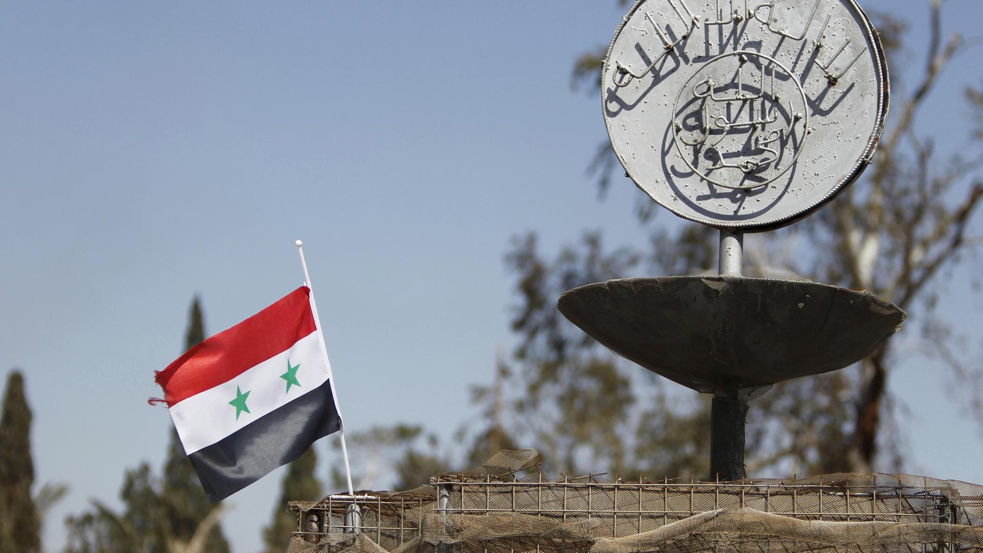 A Syrian national flag flutters next to ISIS slogan