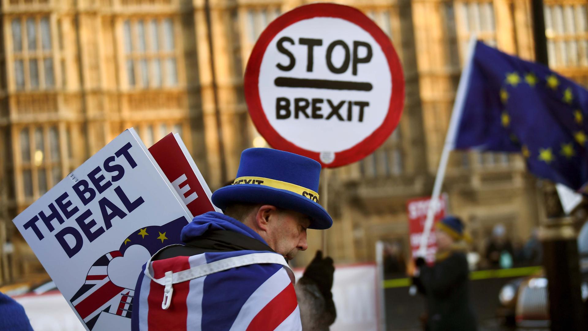 A man with a top hat and UK flag draped around his shoulders holds anti-Brexit protest signs