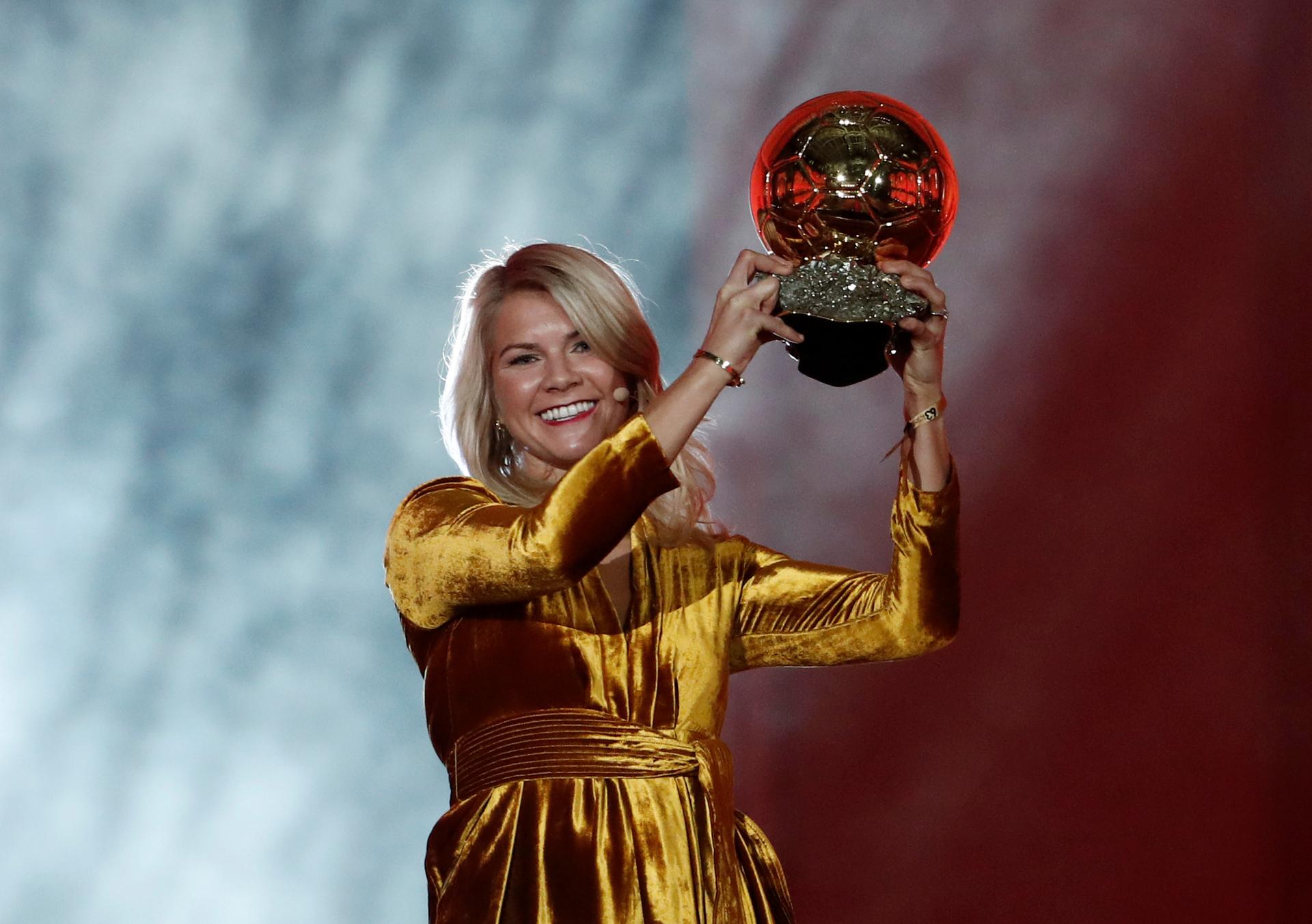 Ada Hegerberg wears a gold dress while holding a gold trophy over her head