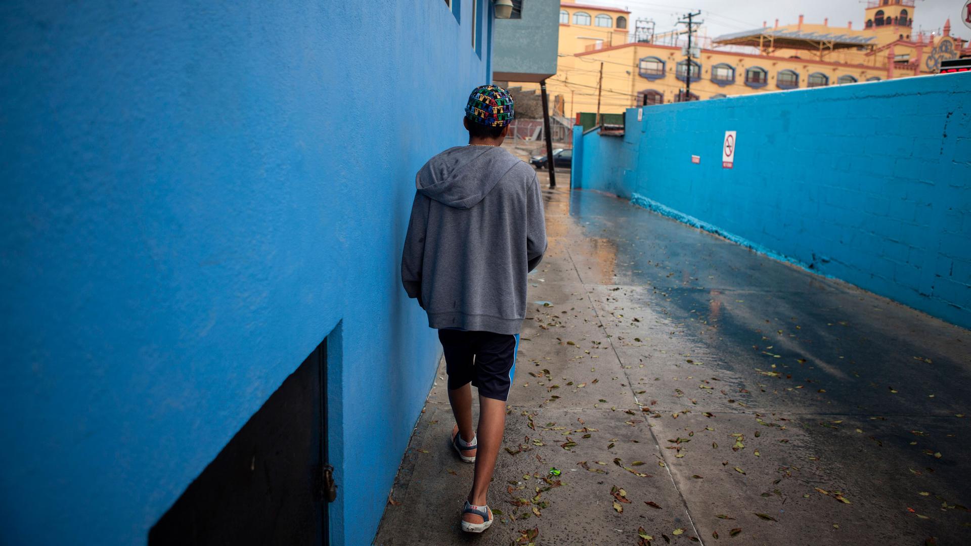 A teenage walks down a driveway next to a bright blue building