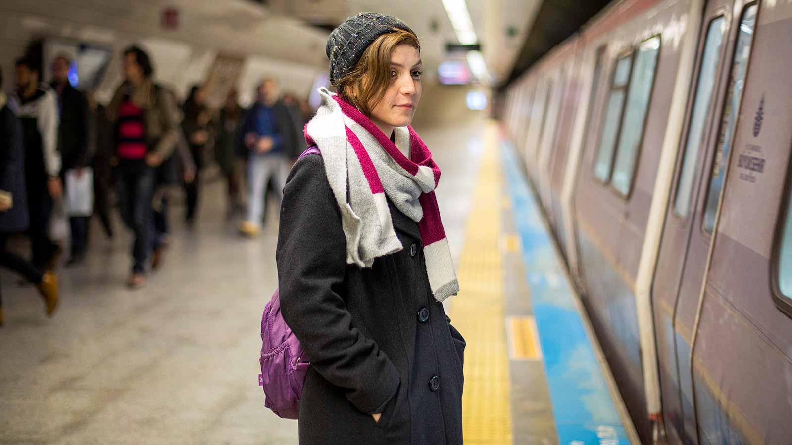 A woman wearing a hat stands on a subway platform