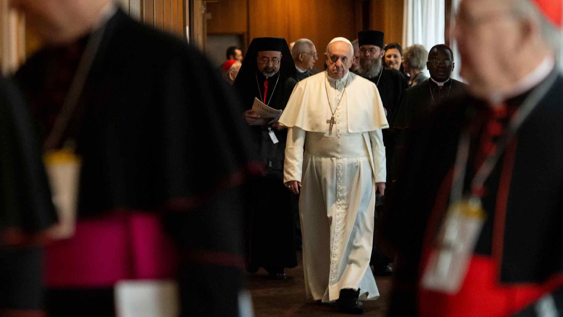 Pope Francis walks through a group of other clergy members