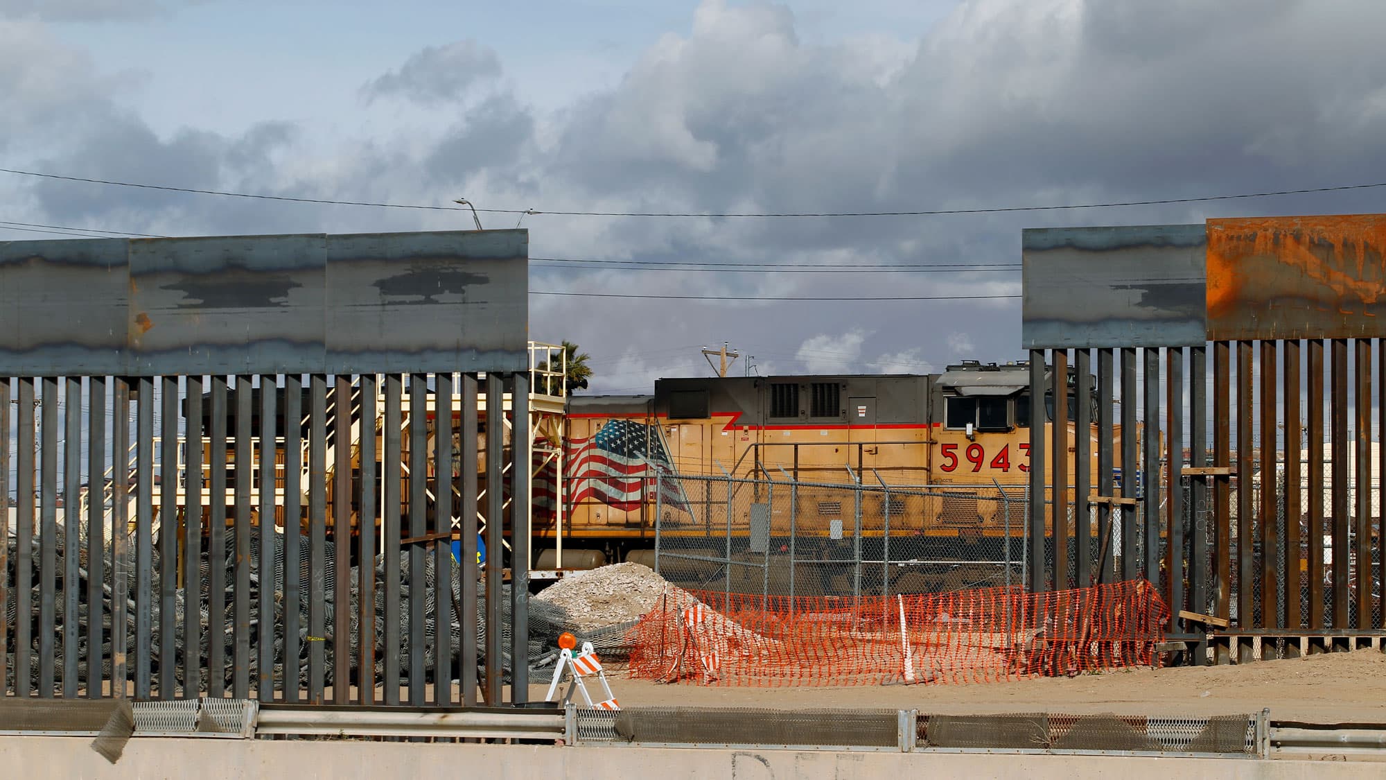 A view showing a section of a metal-slated border fence with a train rolling past in El Paso, Texas, as seen from Ciudad Juarez, Mexico.