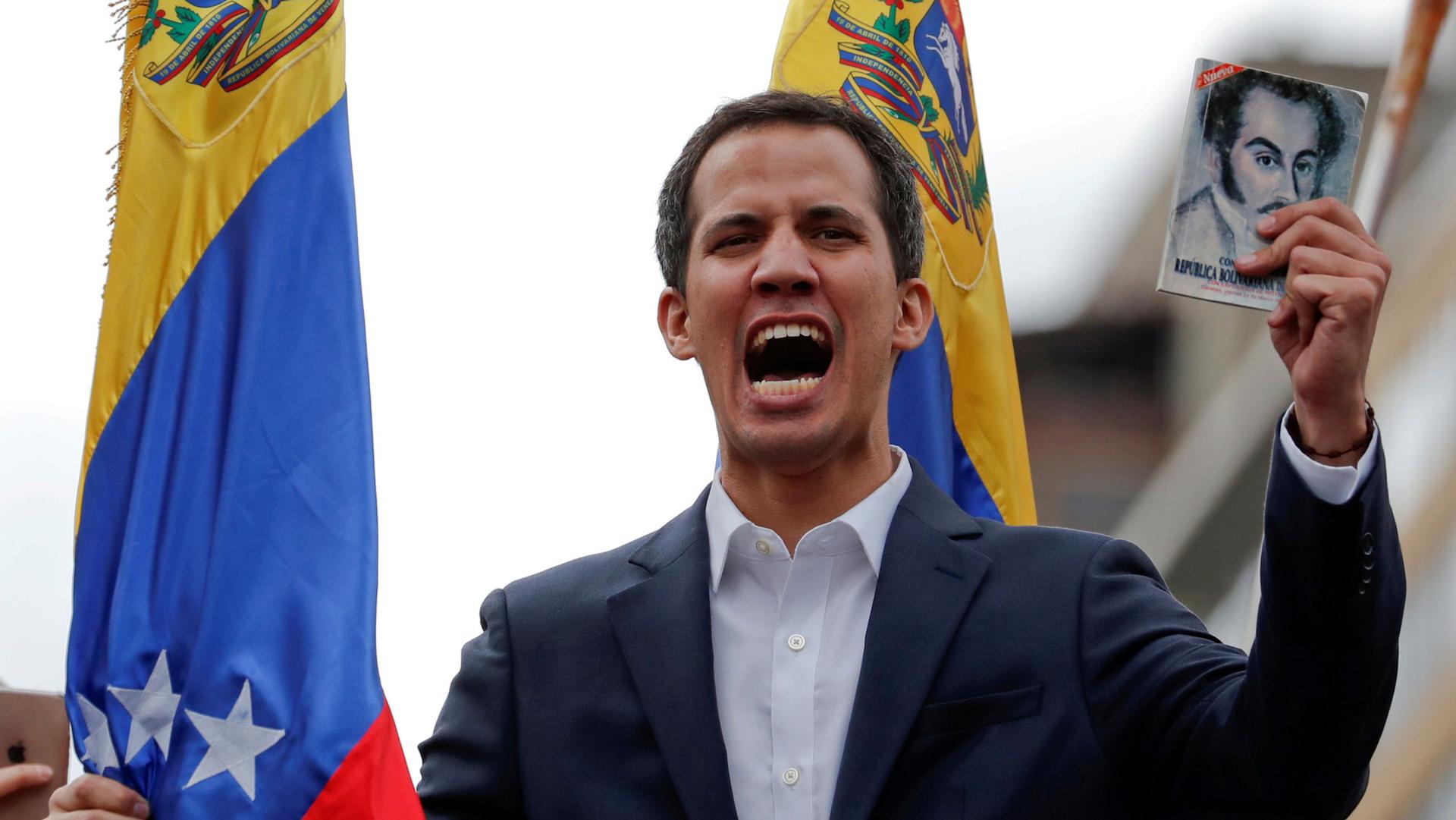 Juan Guaido is shown in a suit jacket and no tie while holding a copy of Venezuelan constitution during a rally in Caracas, Venezuela.