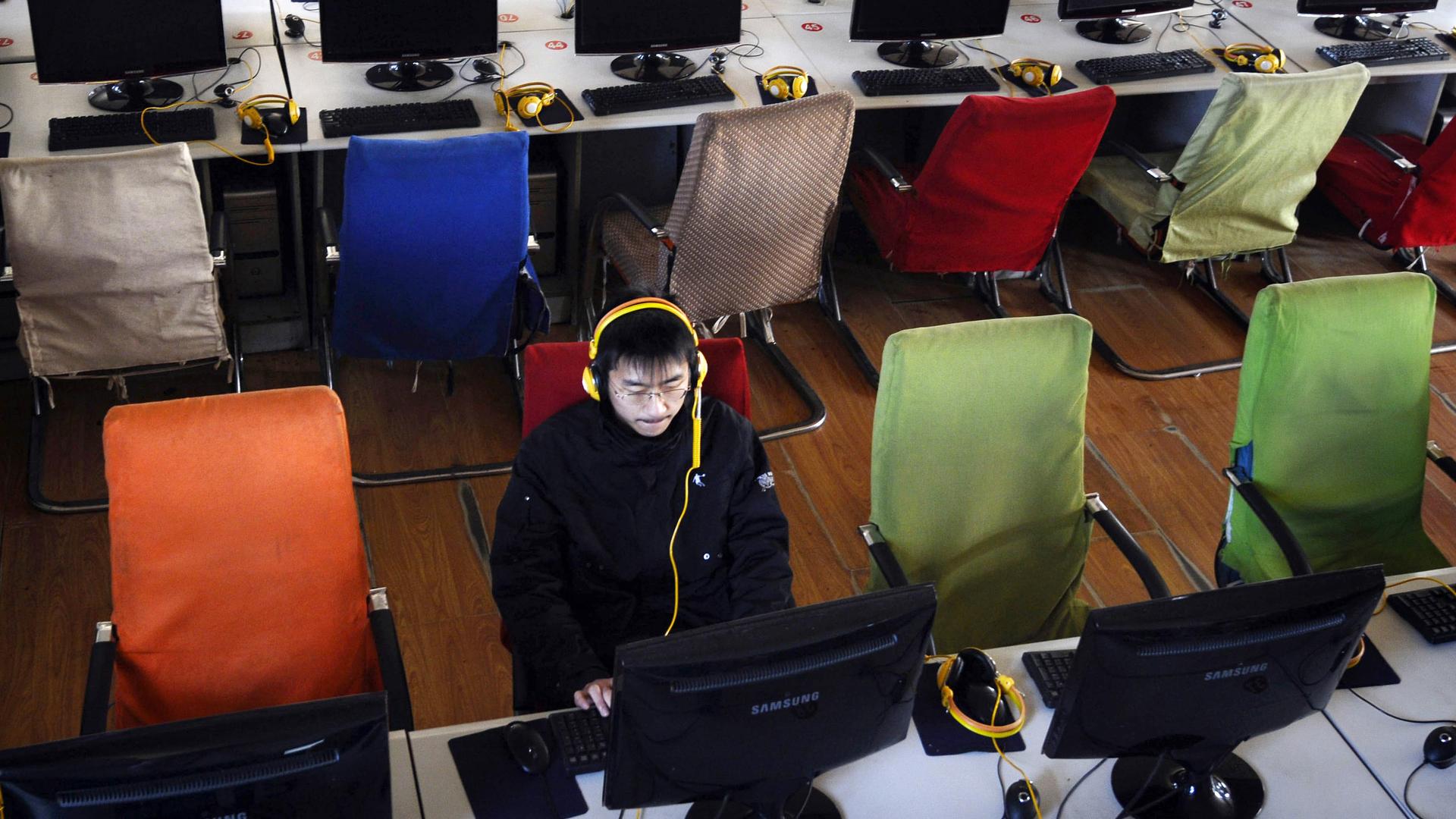 a young Chinese man wears yellow headphones in front of a computer