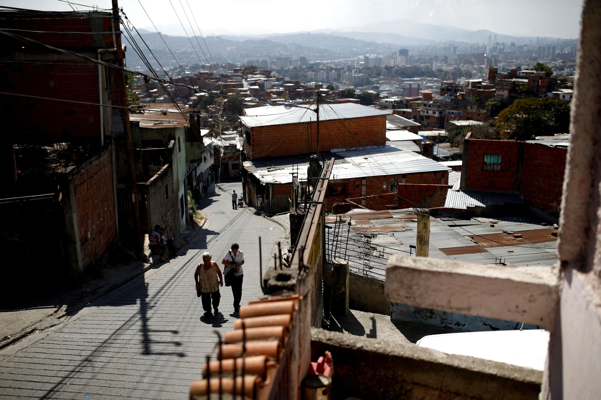 Two women are shown walking up a hilly street in Caracas.