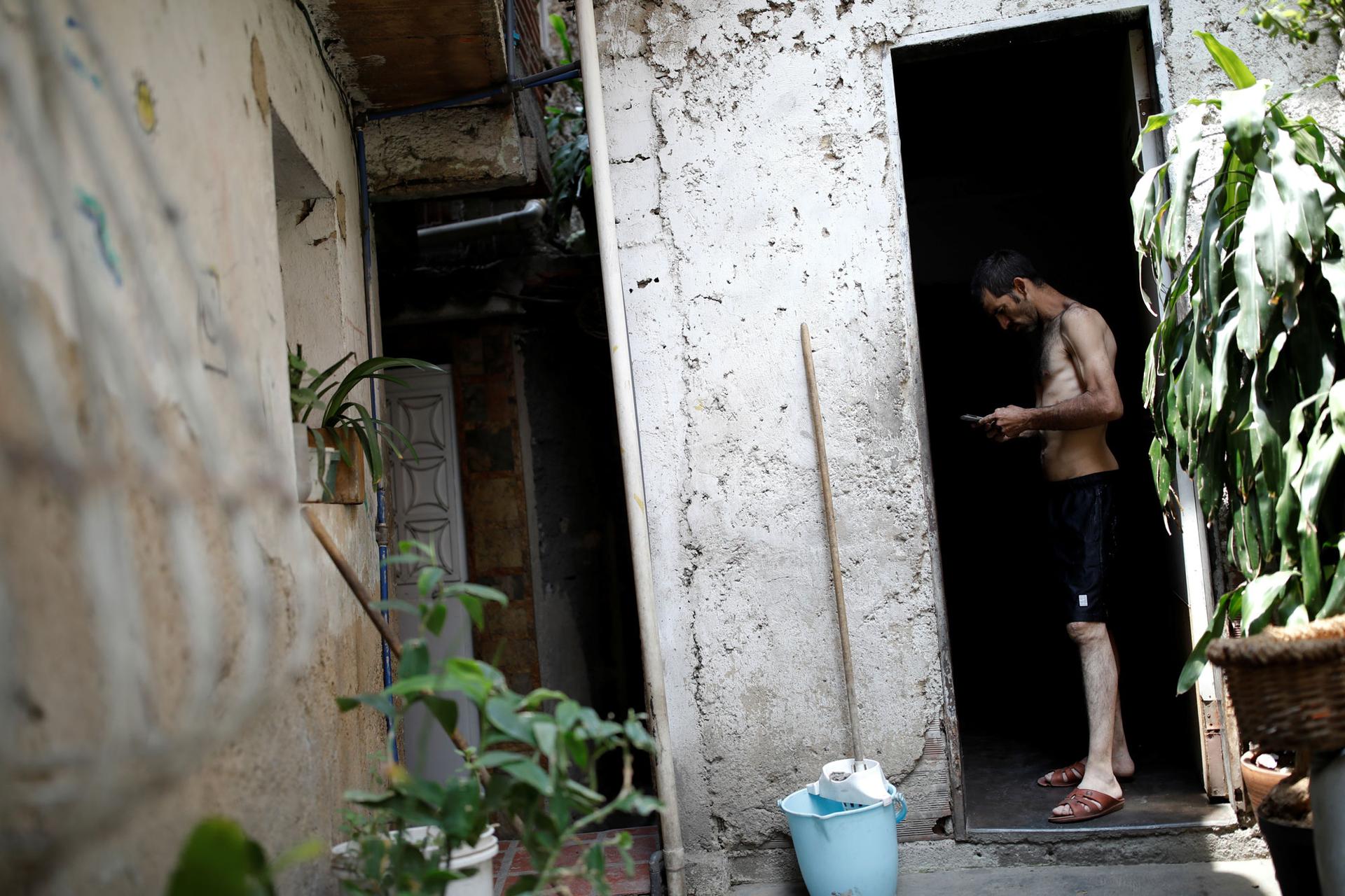 Jorge Perez  is shown standing in a doorway without a shirt on, looking at a phone.