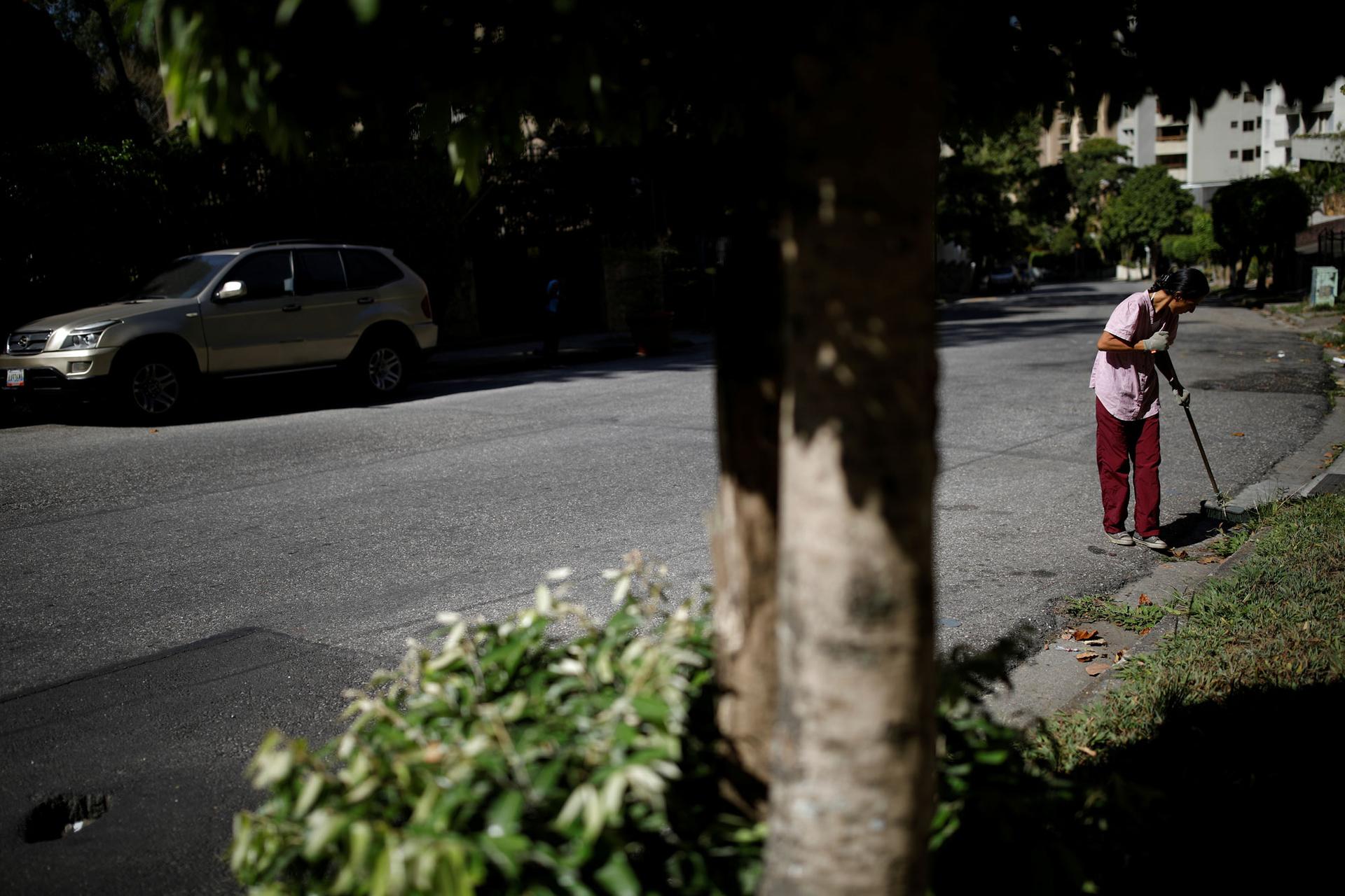 A woman is shown in red pants sweeping the street.