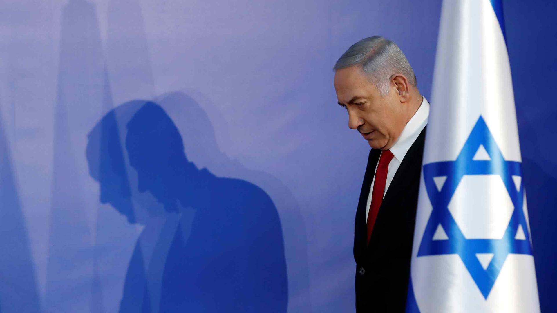 Benjamin Netanyahu stands behind an Israeli flag