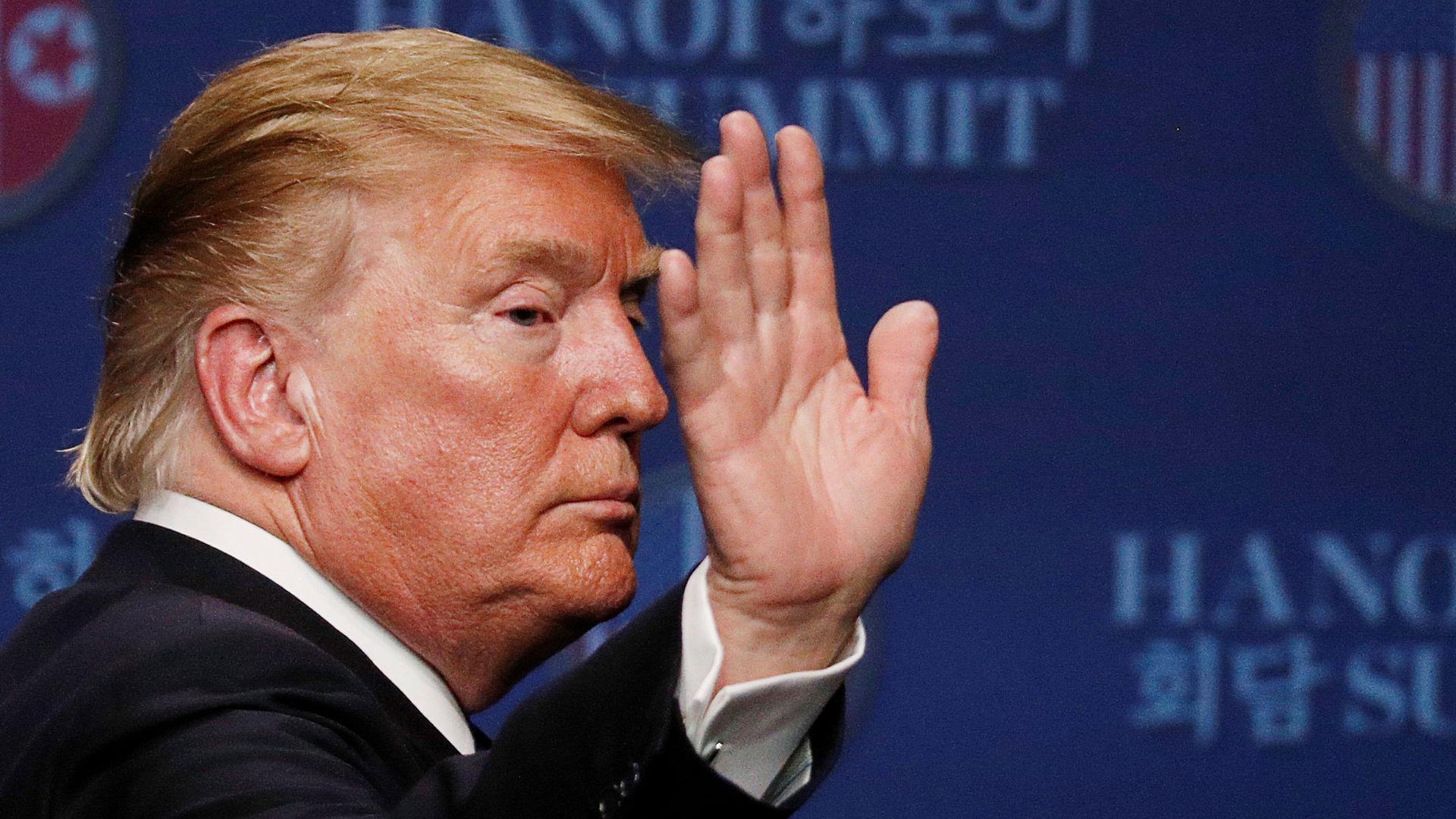 President Donald Trump is shown with his hand up during a news conference in Hanoi, Vietnam.