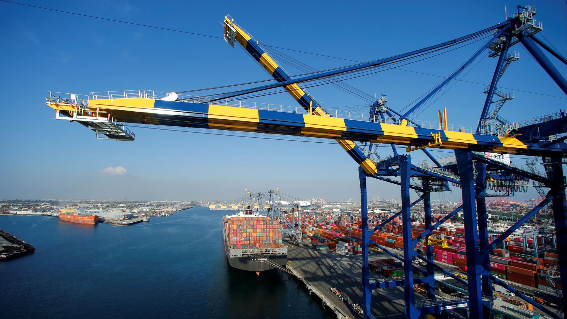 A ship is show loaded with thousands of containers with a blue and yellow crane in the nearground.
