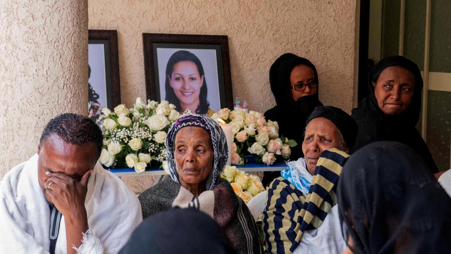 cloaked family members grieve over the deaths of those pictured behind them