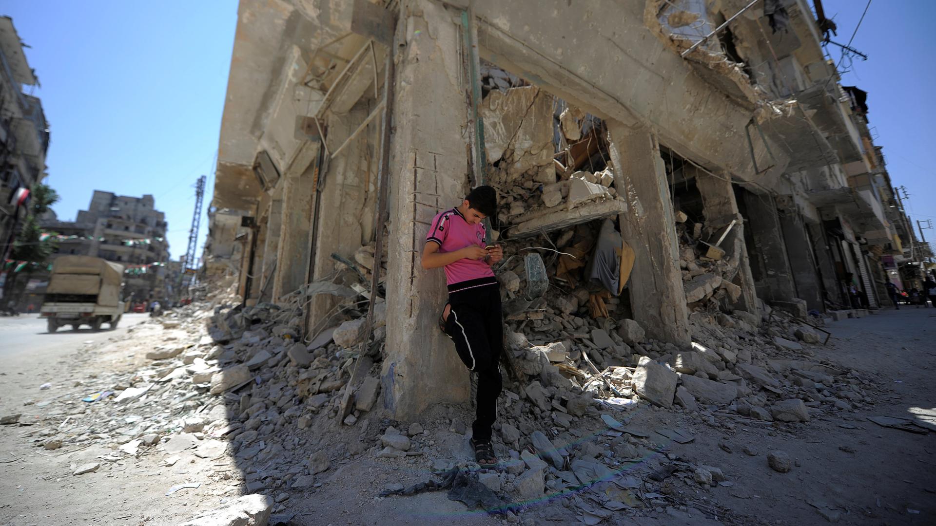 a man in a pink shirt leans against a building reduced to rubble