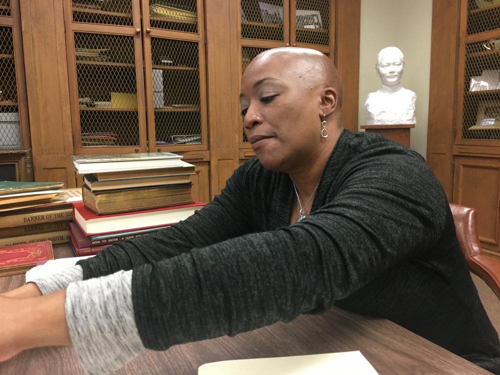 A woman sits at a desk flipping through books.