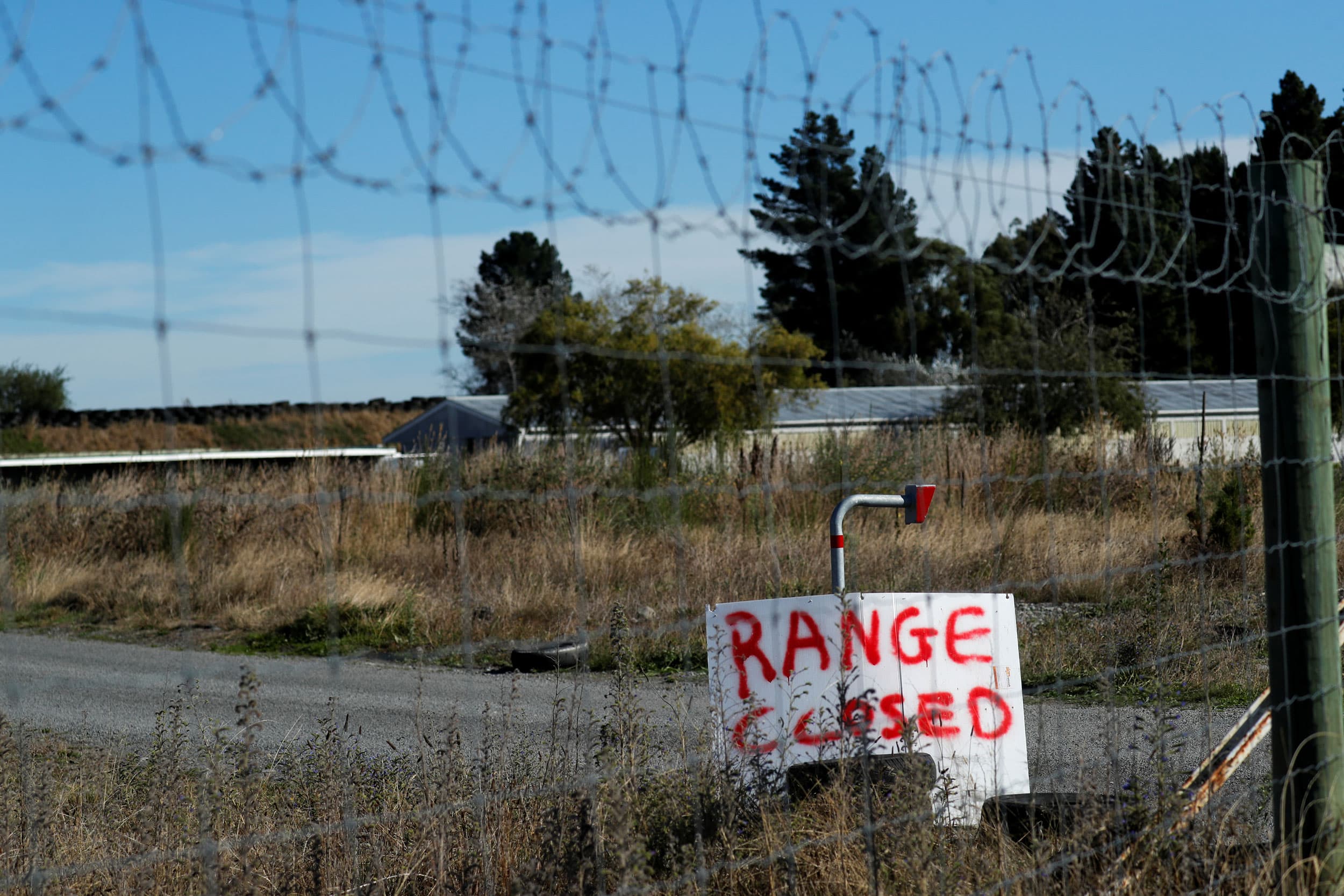 A sign is seen through a chain link fence with a wooden sign reading, 