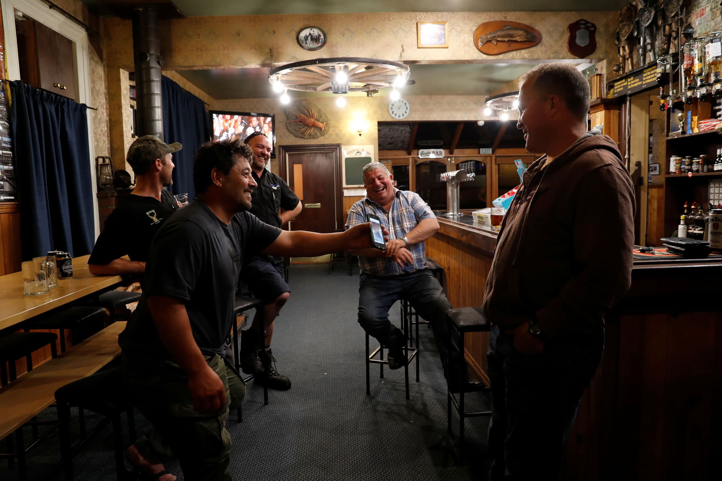 Noel Womersley smiles and shows a picture on his mobile phone to friends in a pub.