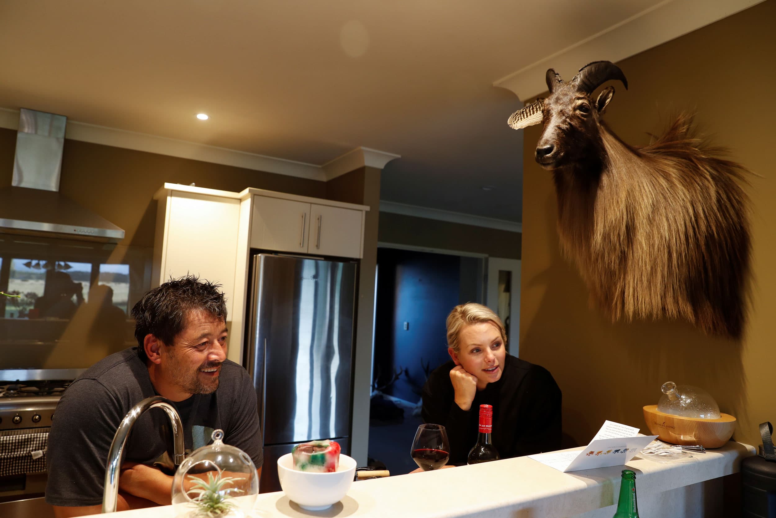 Noel Womersley and his partner Helena are shown sitting at a kitchen counter chatting with a friend.