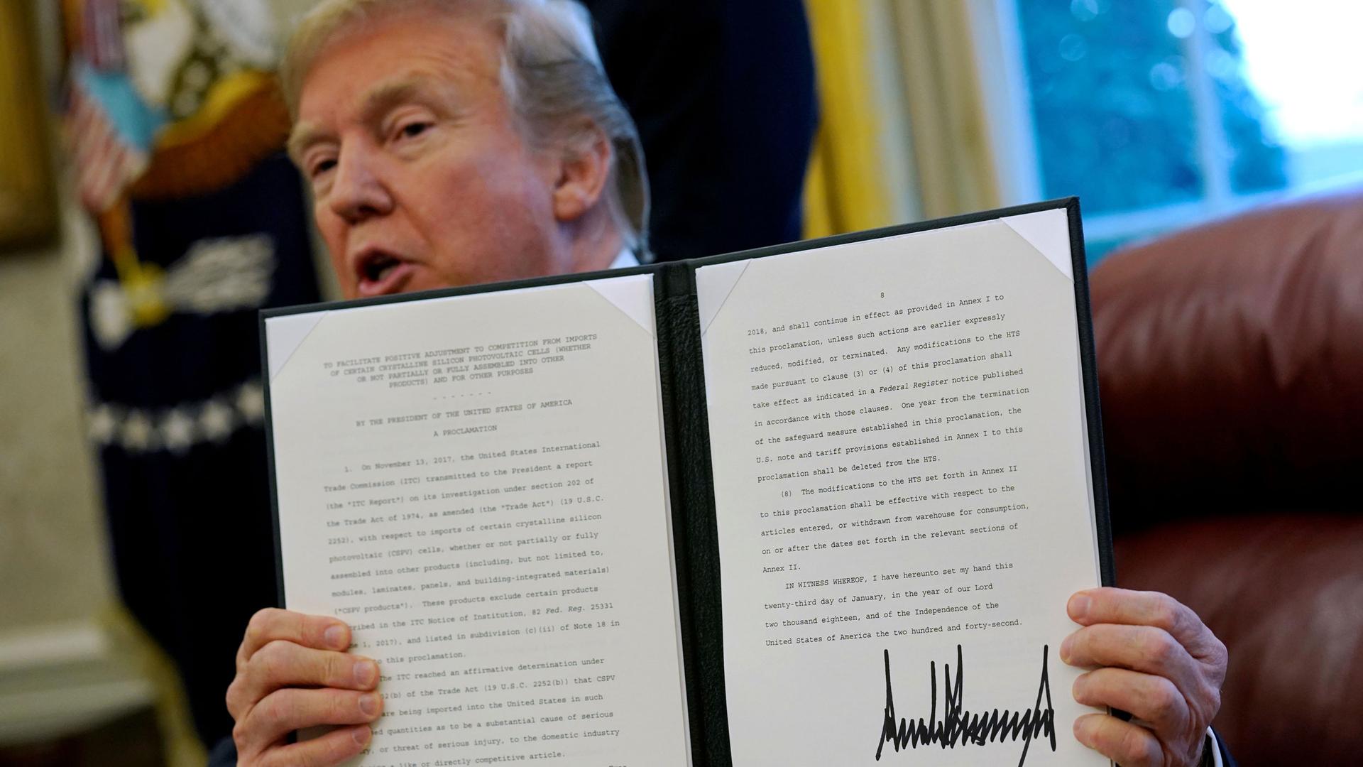 Donald Trump is shown holding.a folder with a directive typed out and his signature.