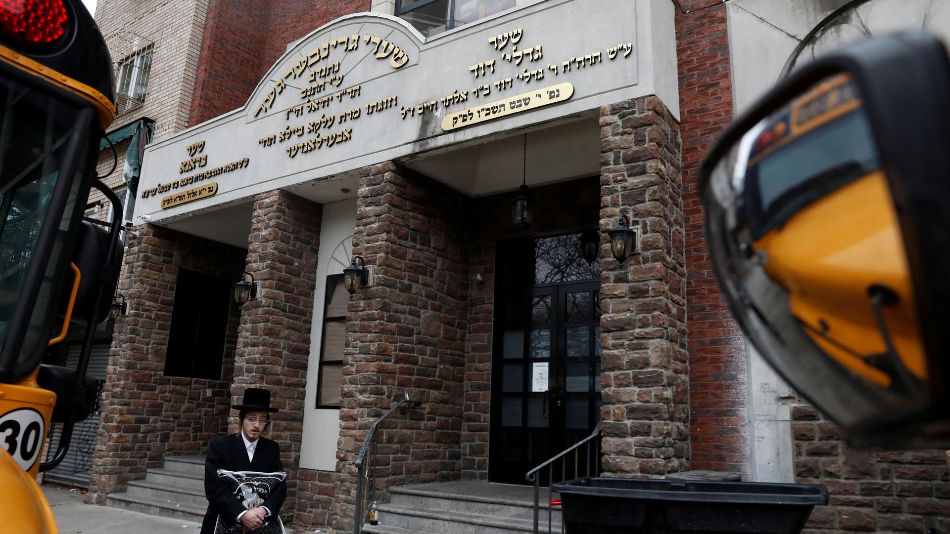 An Orthodox Jewish man is shown walking past the brick facade of the Yeshiva Kehilath Yakov school in Brooklyn.