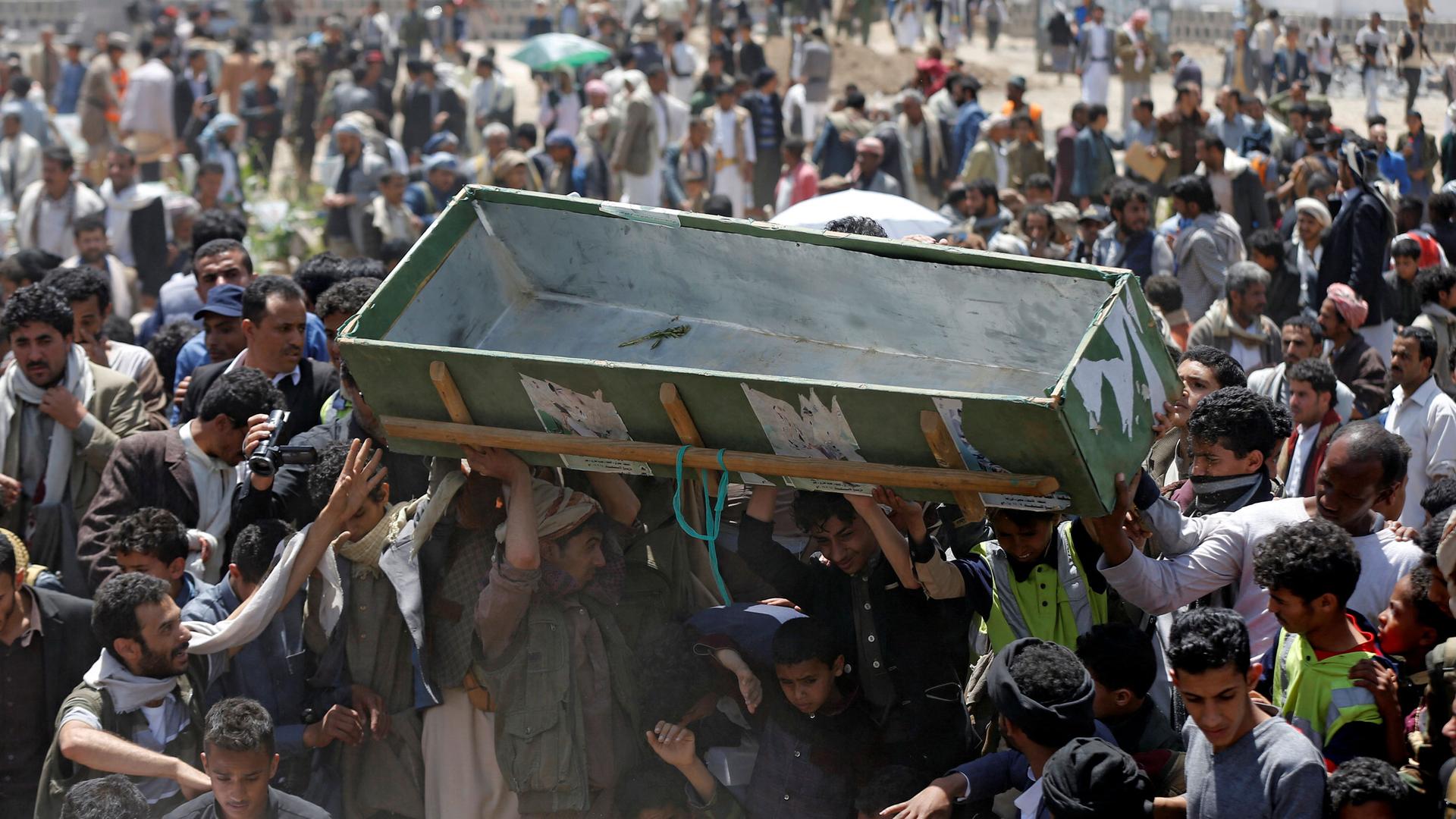 A group of people are shown carrying above their head an empty green coffin.