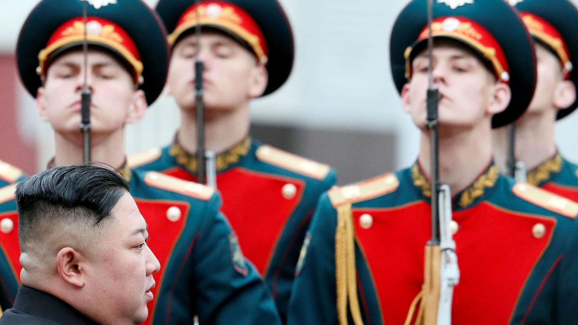 A side profile photo of Kim Jong-un with Russia soldiers in dress uniforms in the background.