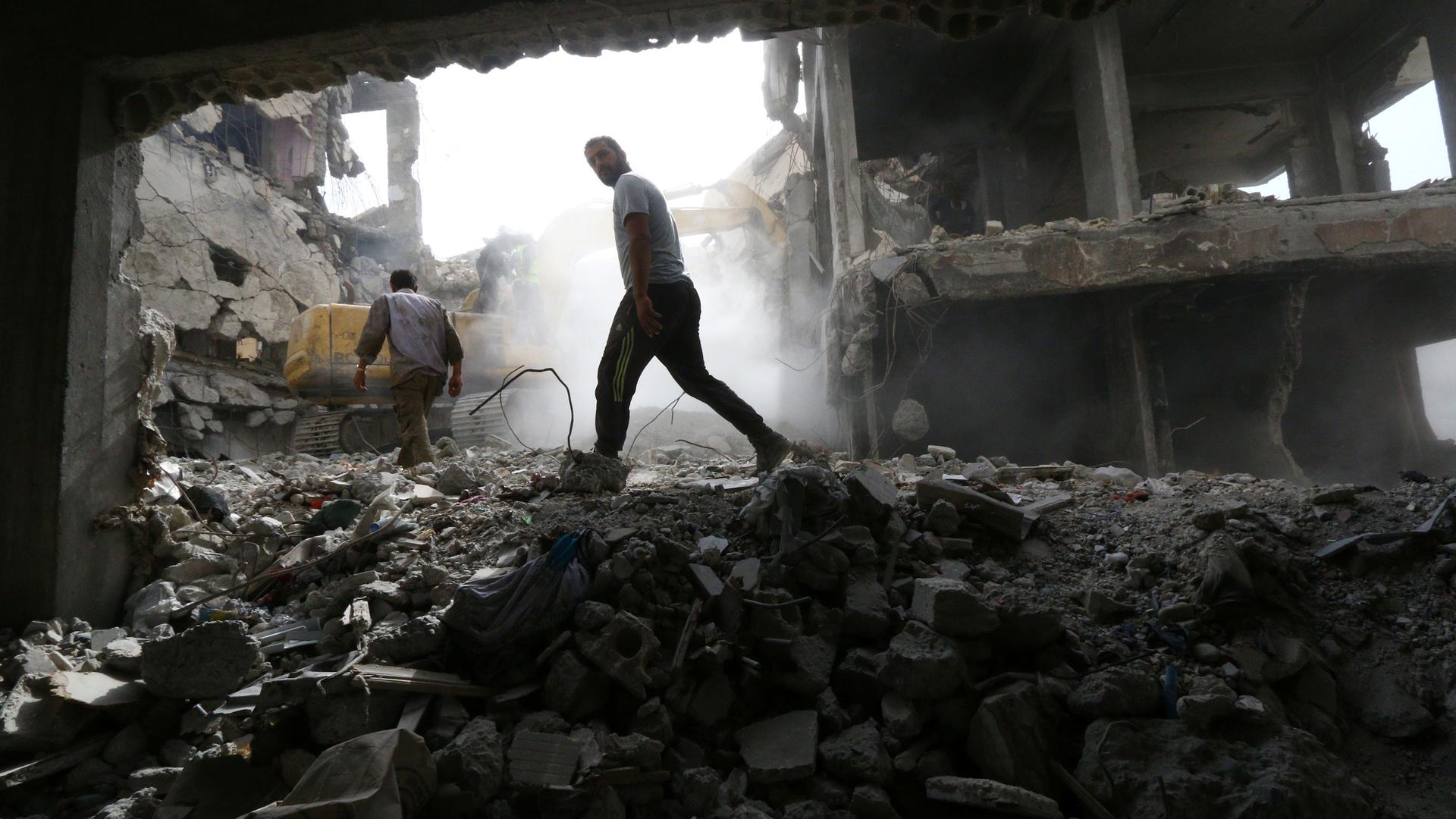 A man is shown walking through the rubble of a destroyed building in Syria.