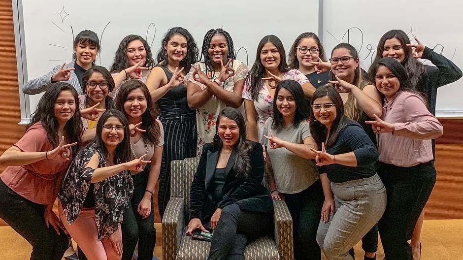 A group of Latina women in front of white boards pose for the camera