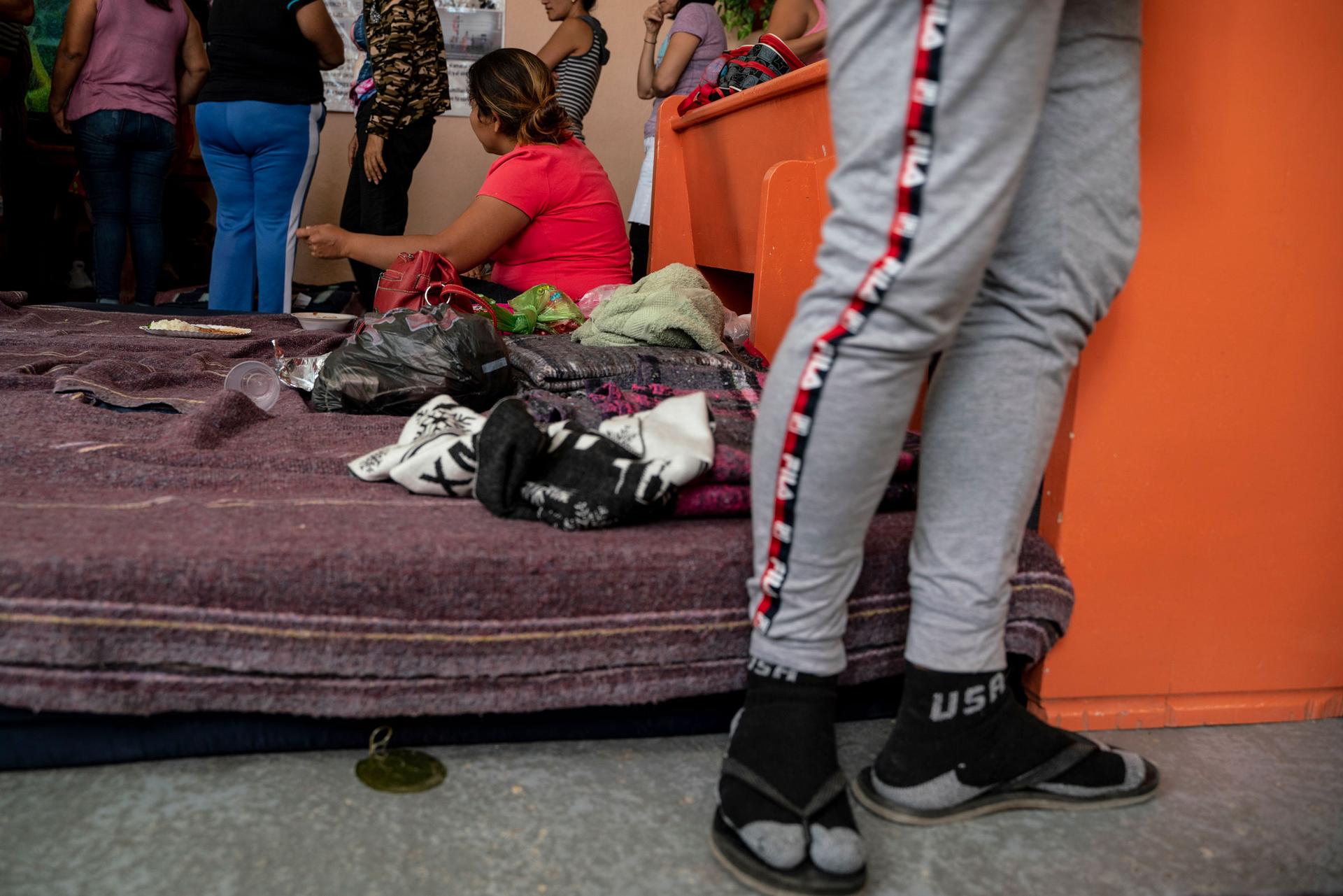 A mattress sits on the floor as people stand around a room.