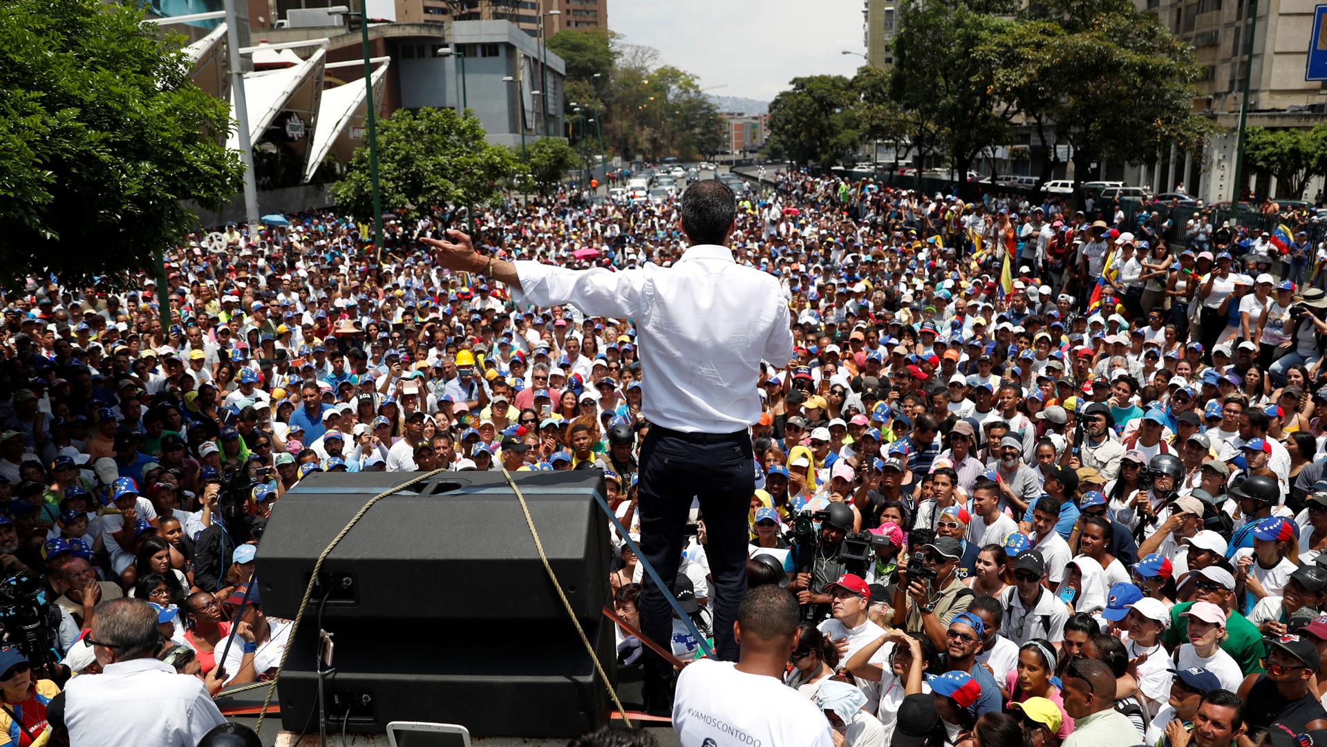 Venezuelan opposition leader Juan Guaidó is photographed from behind speaking out to hundreds of supporters.