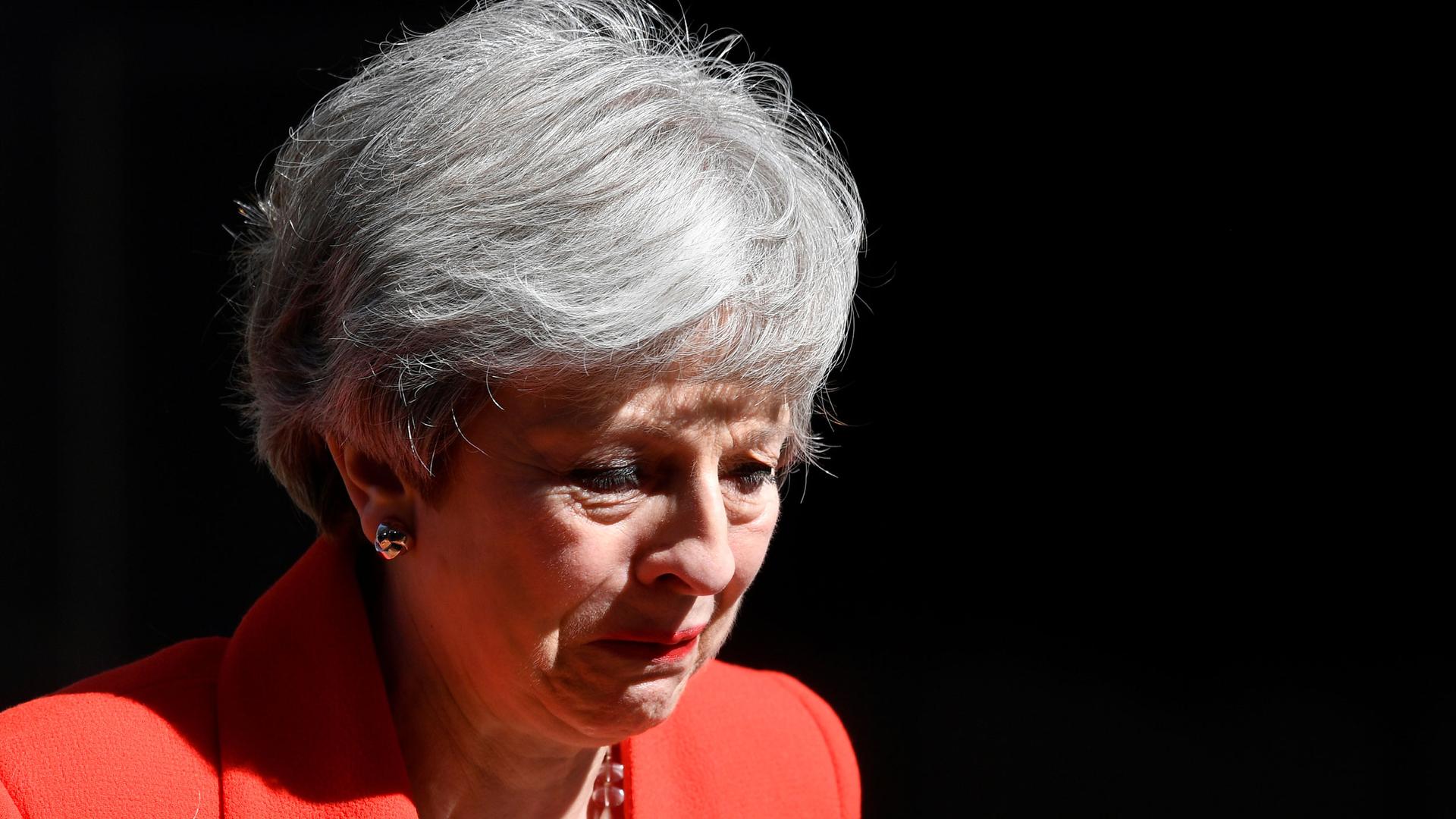 A close-up photograph of British Prime Minister Theresa May is shown with an emotional reaction.