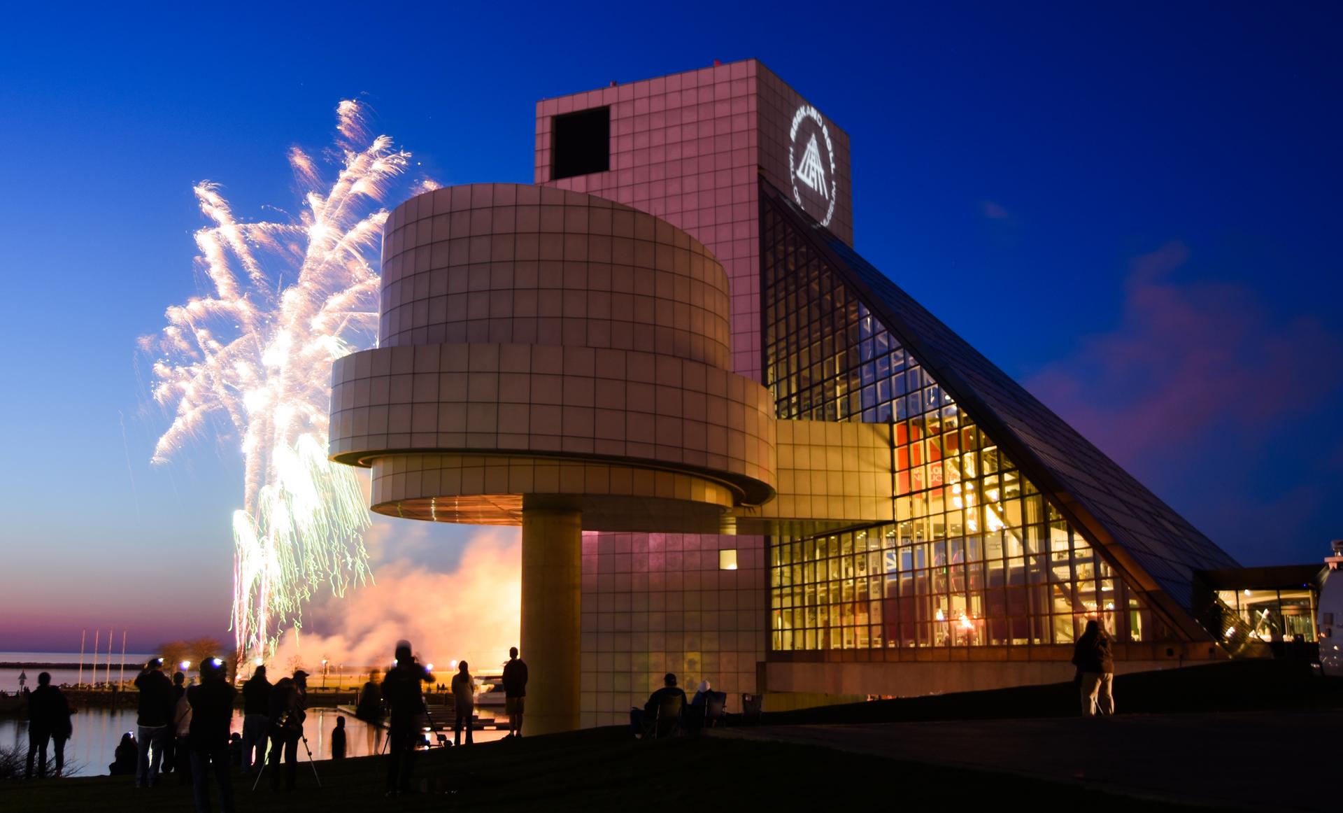 Fireworks flash next to the Rock and Roll Hall of Fame at night.