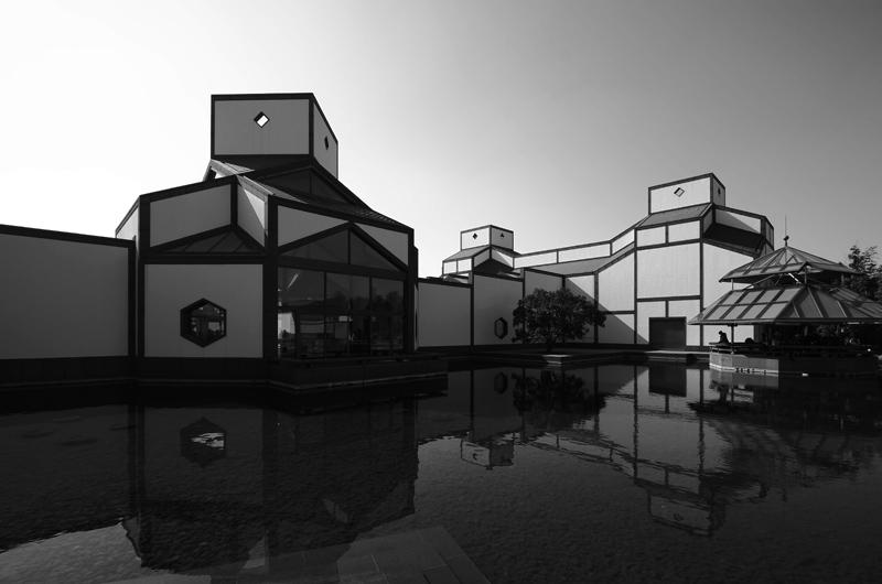 A black and white photo of the Suzhou Museum next to water.