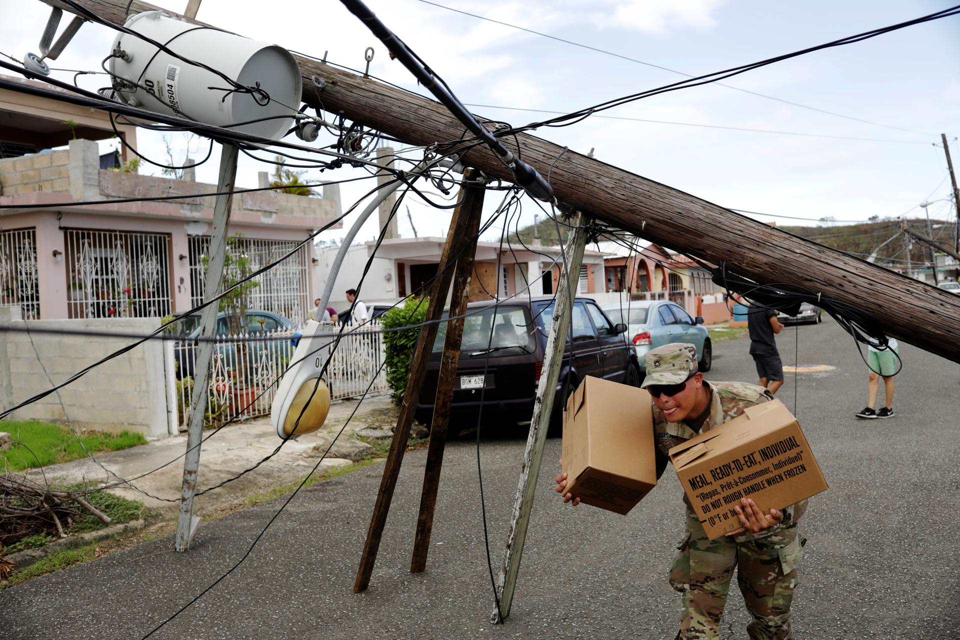 A member of the Puerto Rican National Guard dodges downed power cables as he hands out food and water
