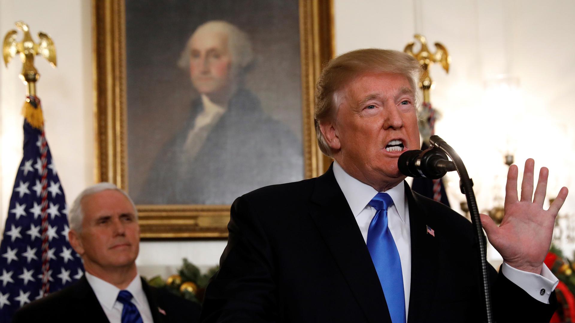 President Donald Trump stand with his hand in the air at a podium at the White House.