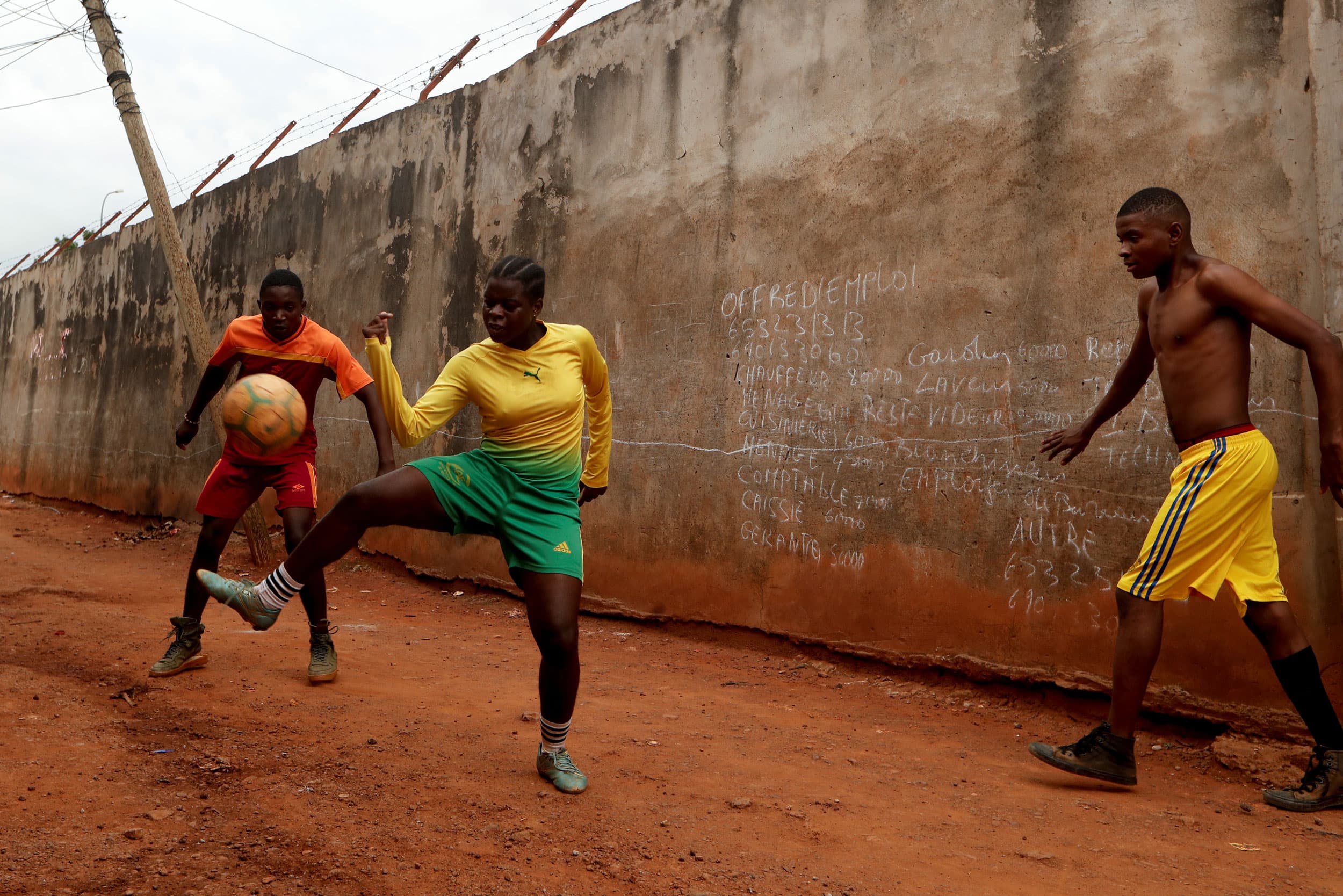 A young woman is shown juggling a soccer ball with two youn men.