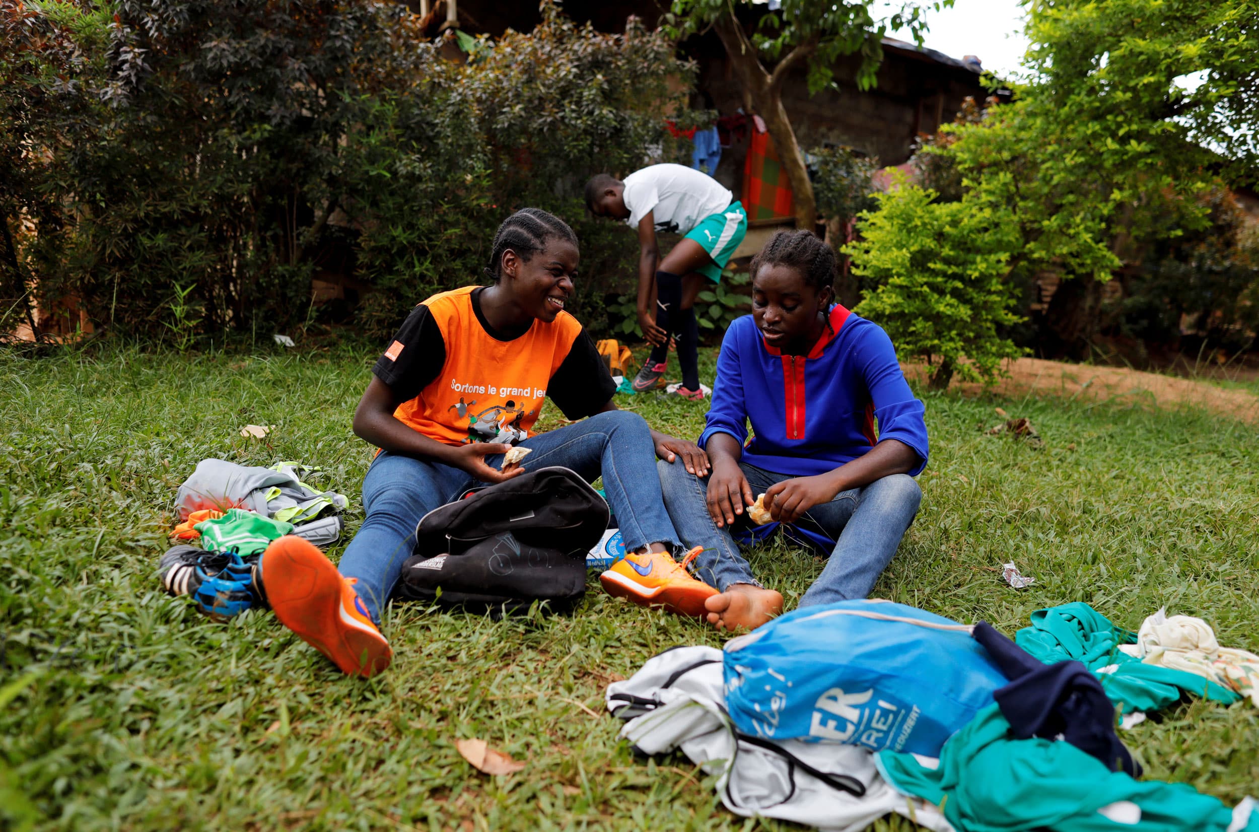 Two young women are shown sitting in the grass smiling.