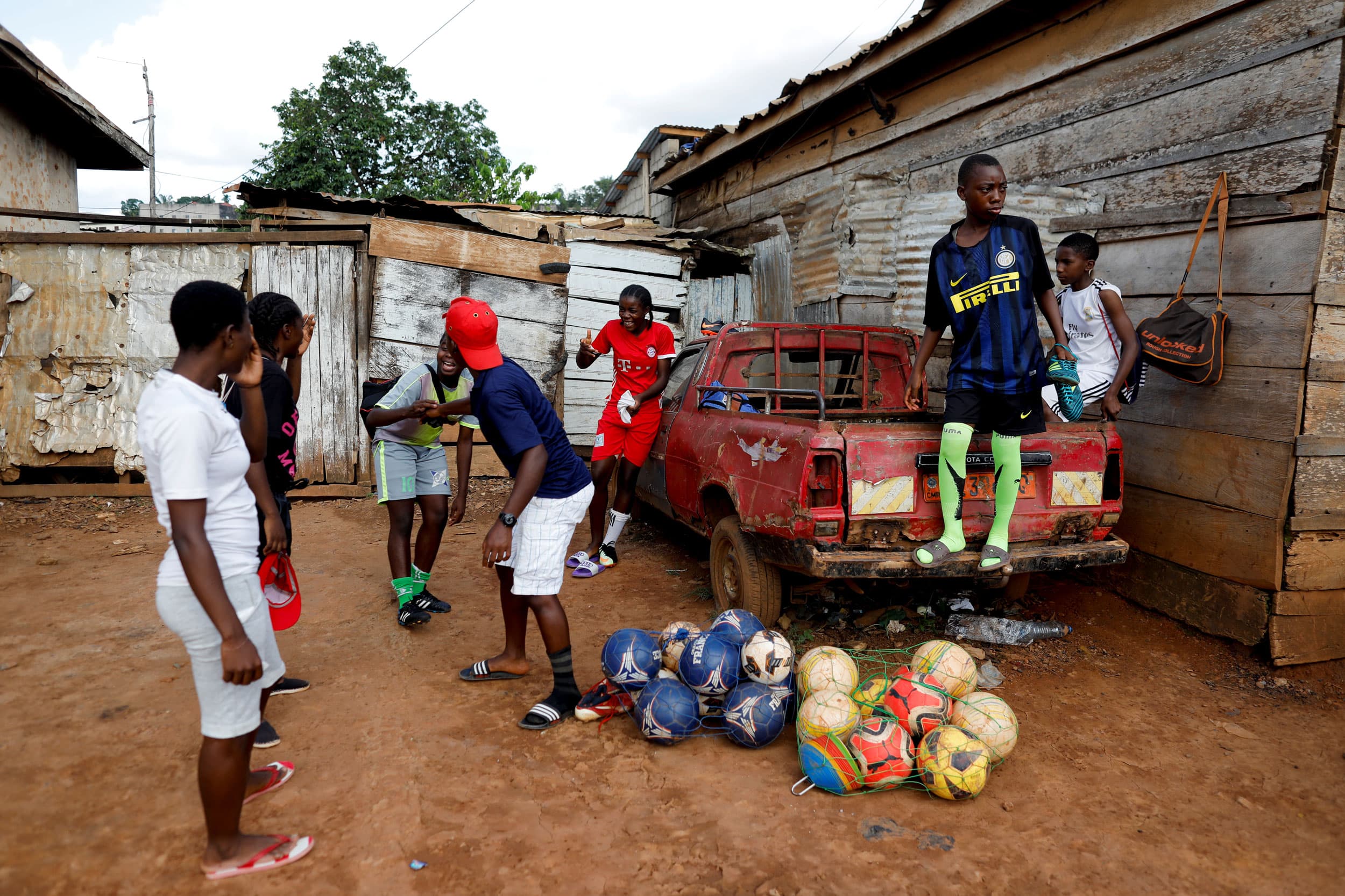 A group of young people are shown standing around a red pickup truck laughing.