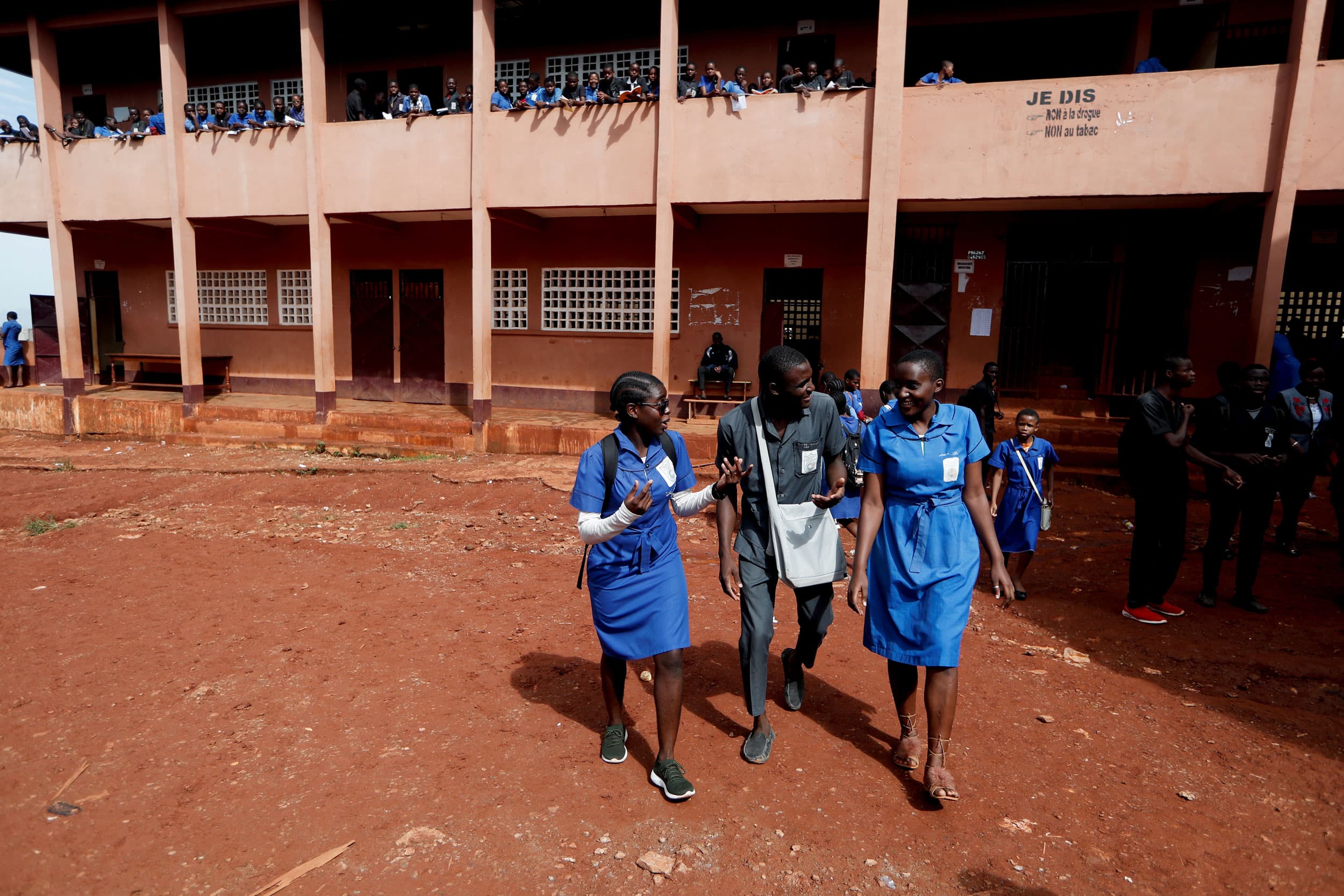 Two young women are shown walking on either side of a young man talking.