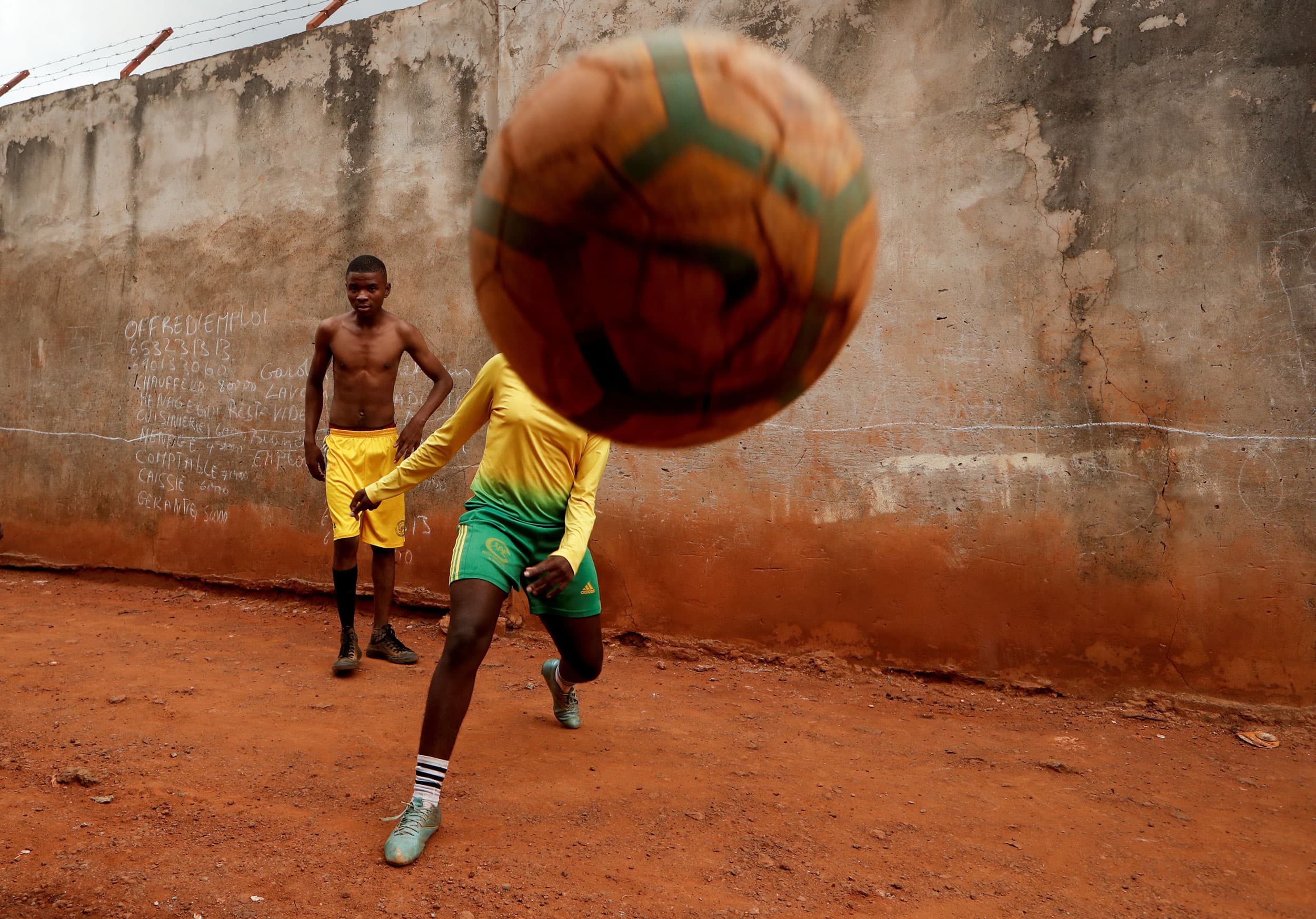 A young woman is shown kicking a soccer ball directly at the camera.