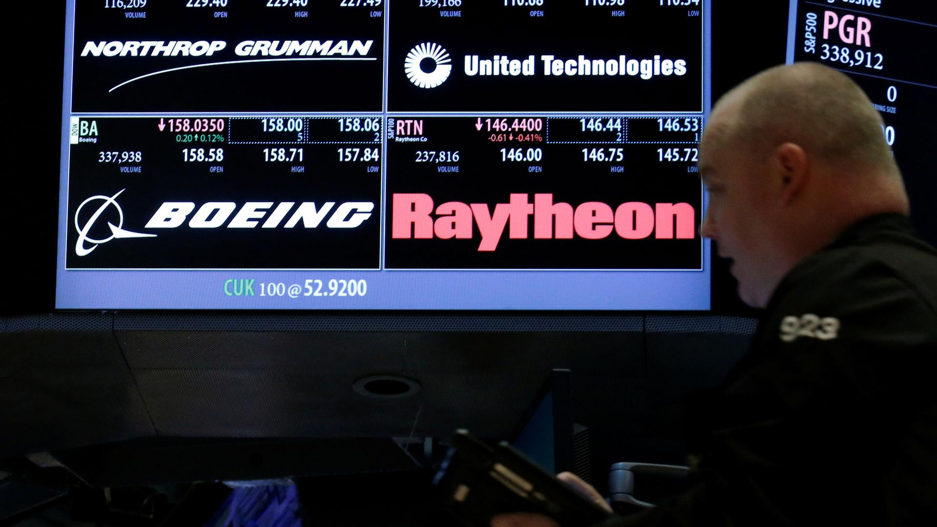 A man is shown in soft focus in the nearground with a stock trading electronic board in the background.