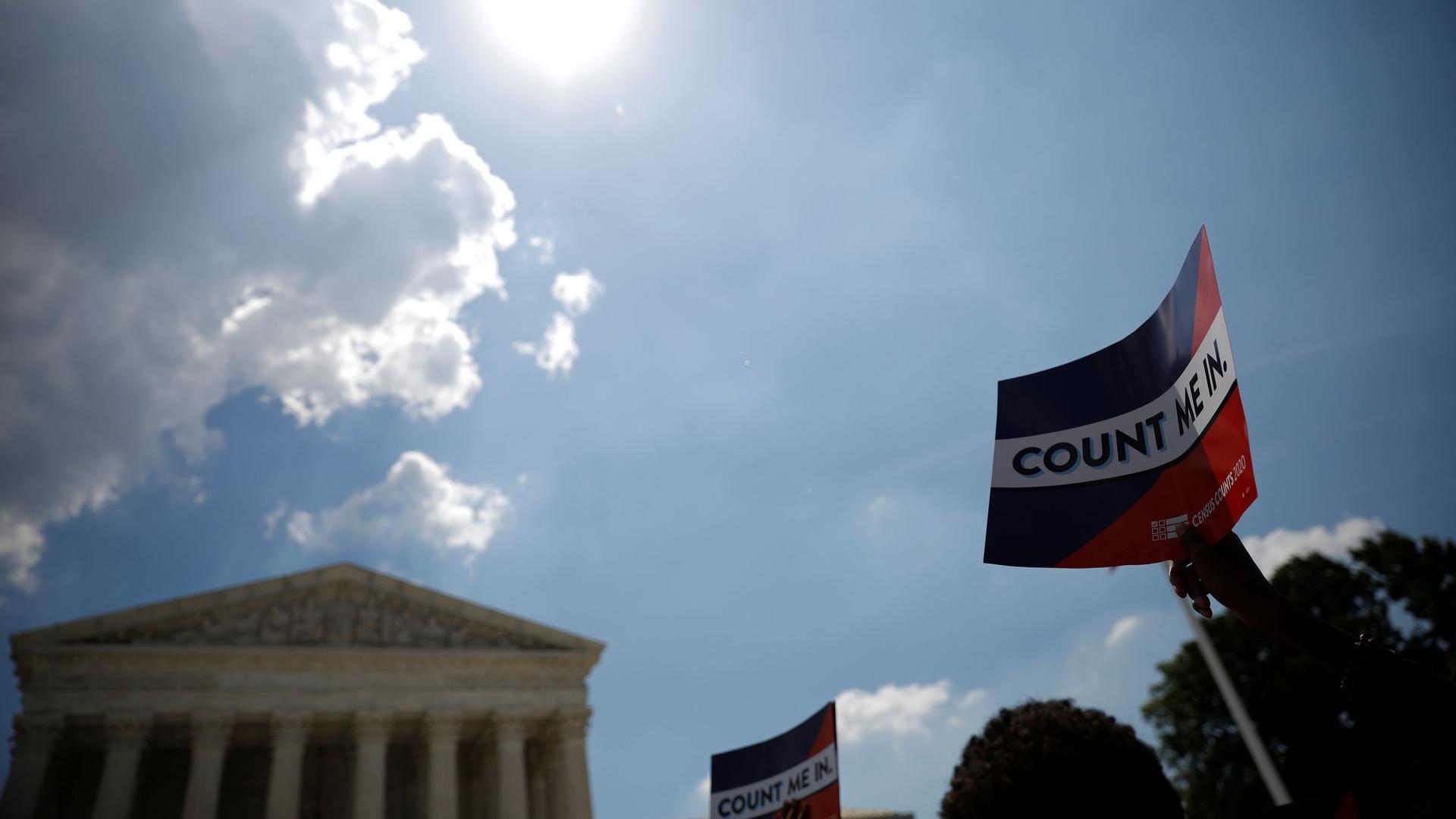 The facade of the Supreme Court building is seen in the background with a placard raised in the nearground with the words "Count Me In" printed on it.