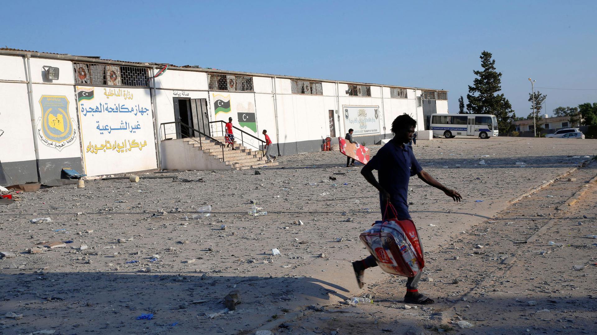 A migrant is shown walking with a bag across a dirt road.