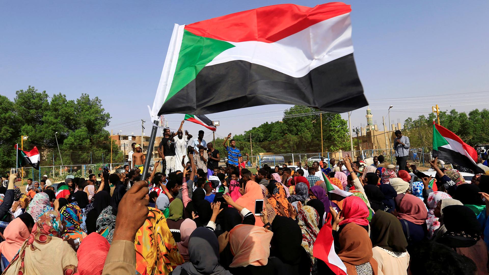 People wave Sudaneses flag and dozens of people raise their hands in celebration