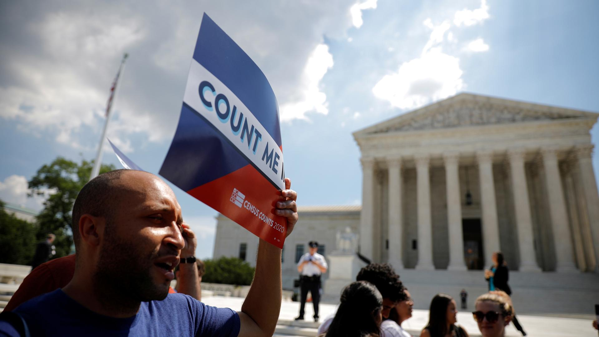 A man stands in front of the US Supreme Court building holding a sign that says "Count me"