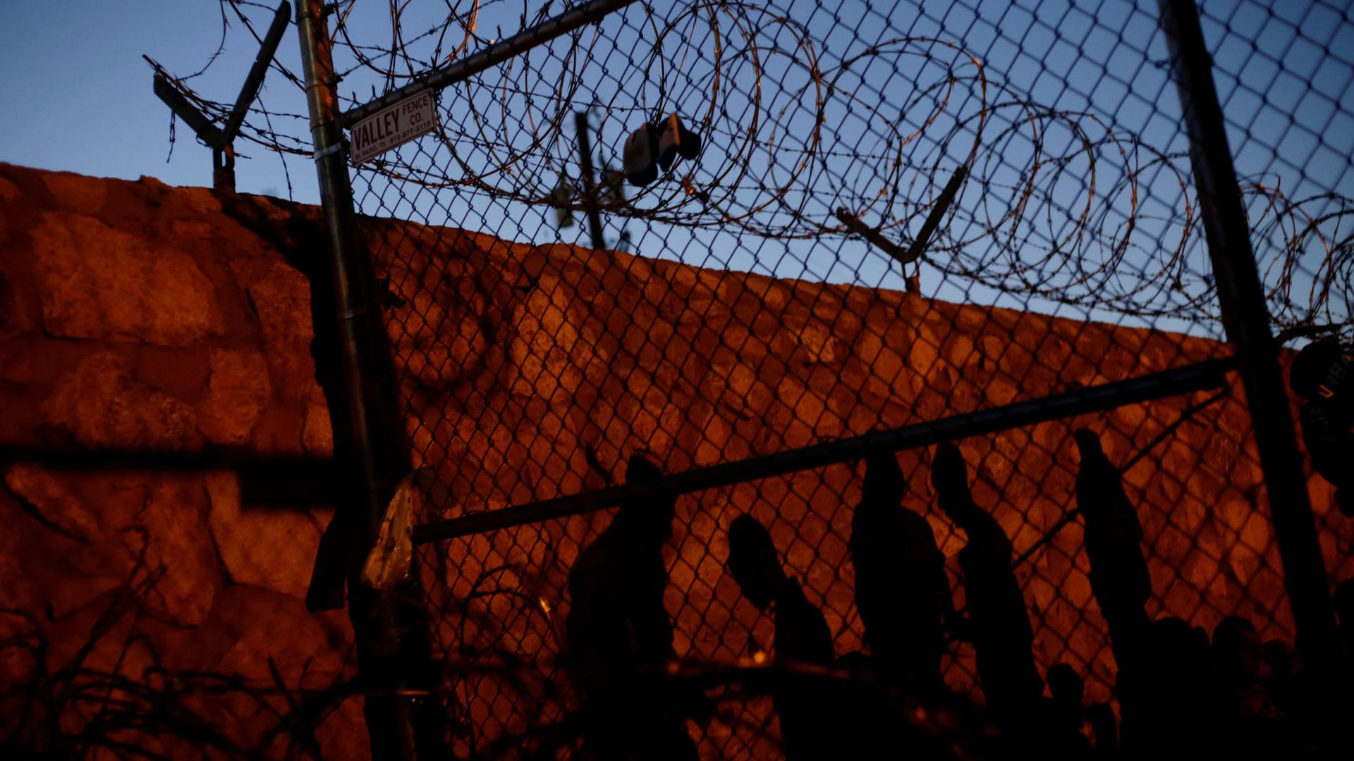 The shadows of five people are shown on a wall with a chainlink fence in the nearground.